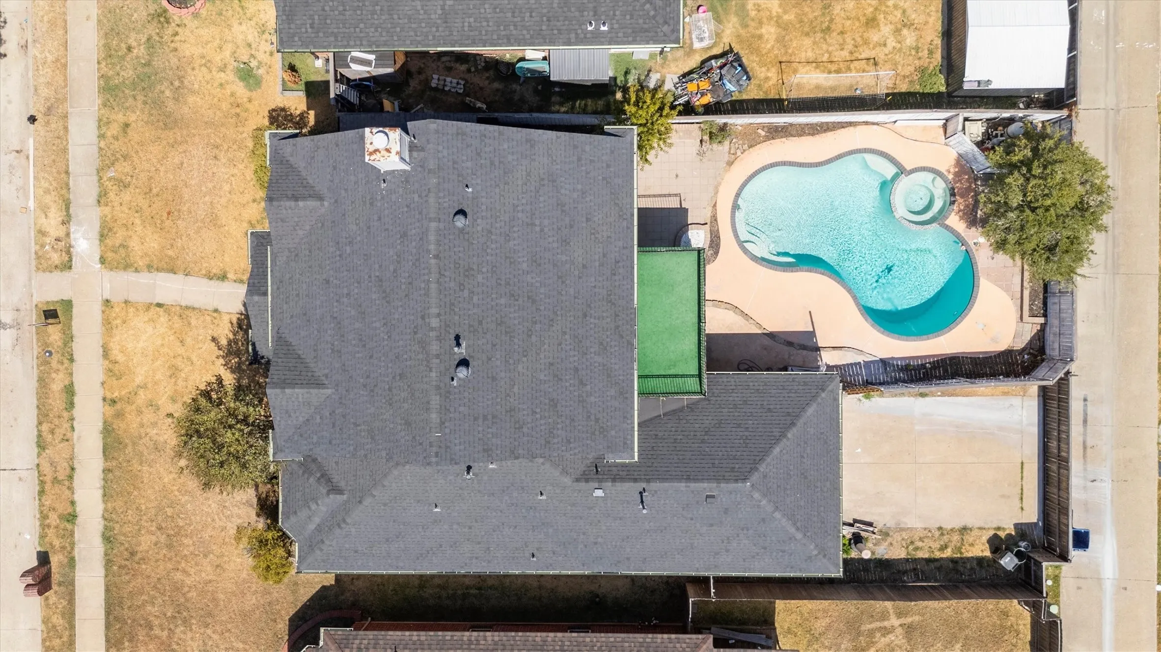 Asphalt shingle roof, chimney, concrete-paved outdoor area, freeform swimming pool, integrated spa