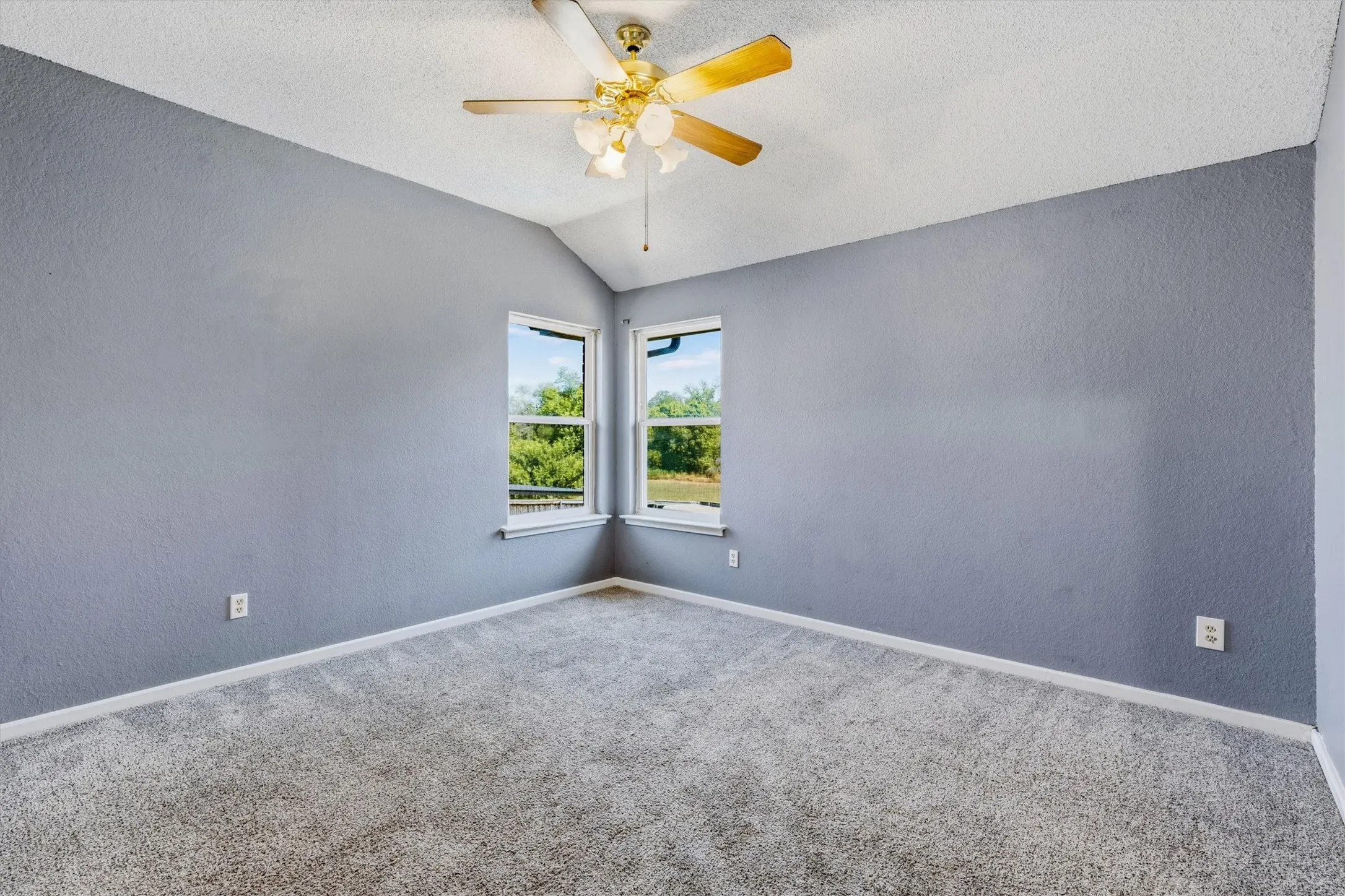 Vaulted ceiling, ceiling fan with integrated lighting, two windows, wall-to-wall carpeting, and light-toned wall finish