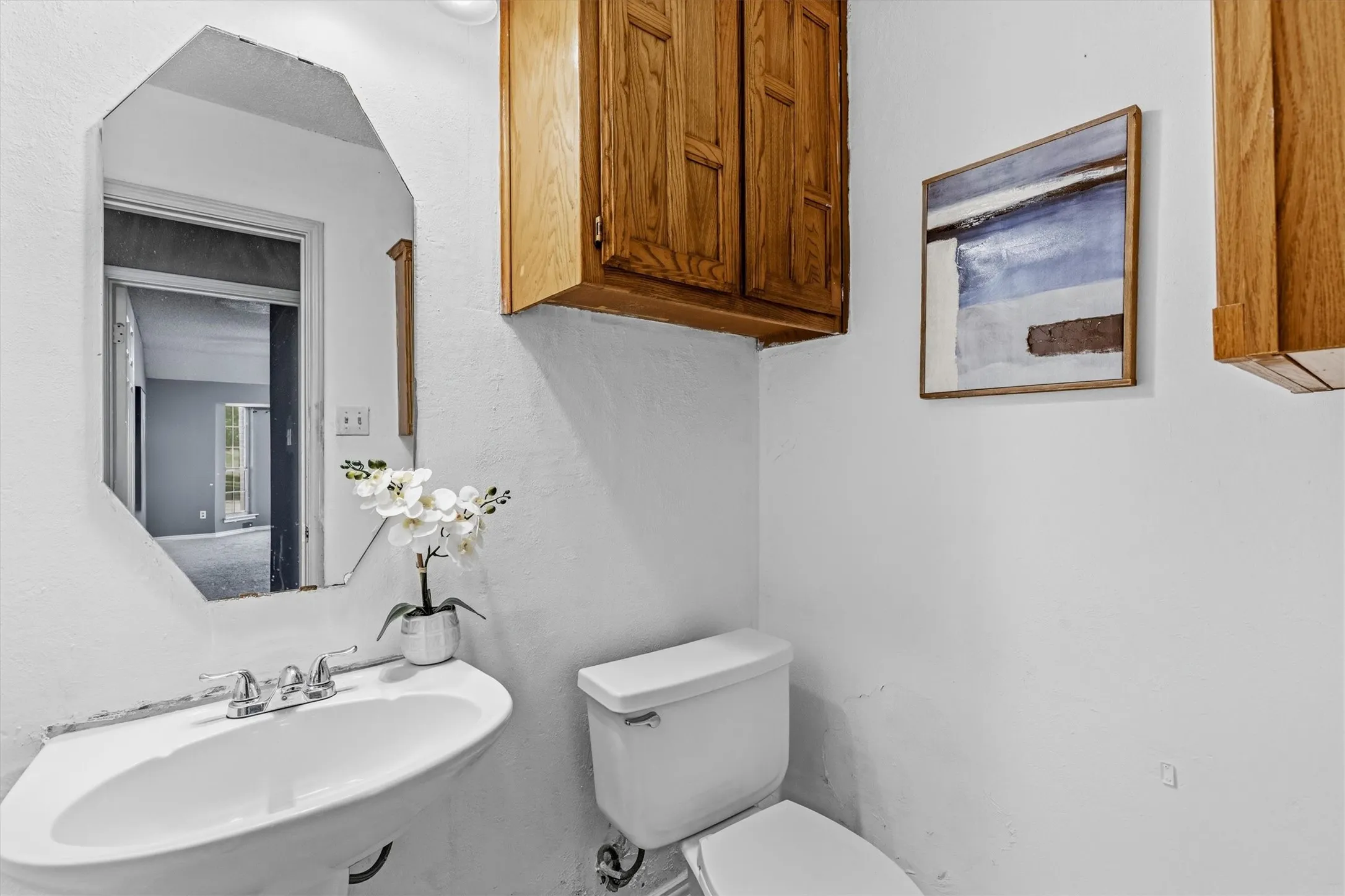 Pedestal sink with chrome faucet, octagonal wall-mounted mirror, and wood-finish cabinetry