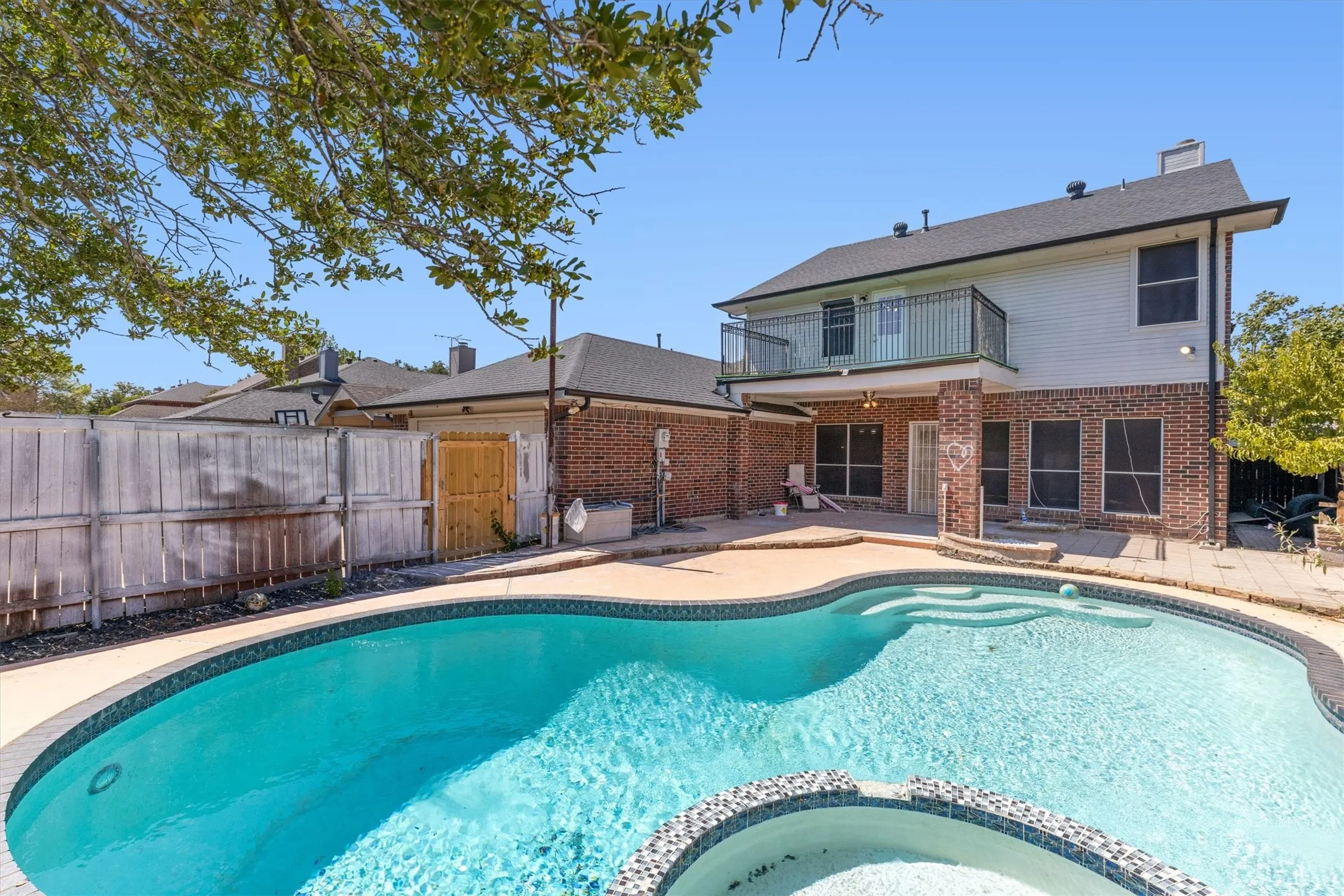 Expansive backyard featuring a free-form pool, integrated spa, and an upper-level balcony with black metal railing