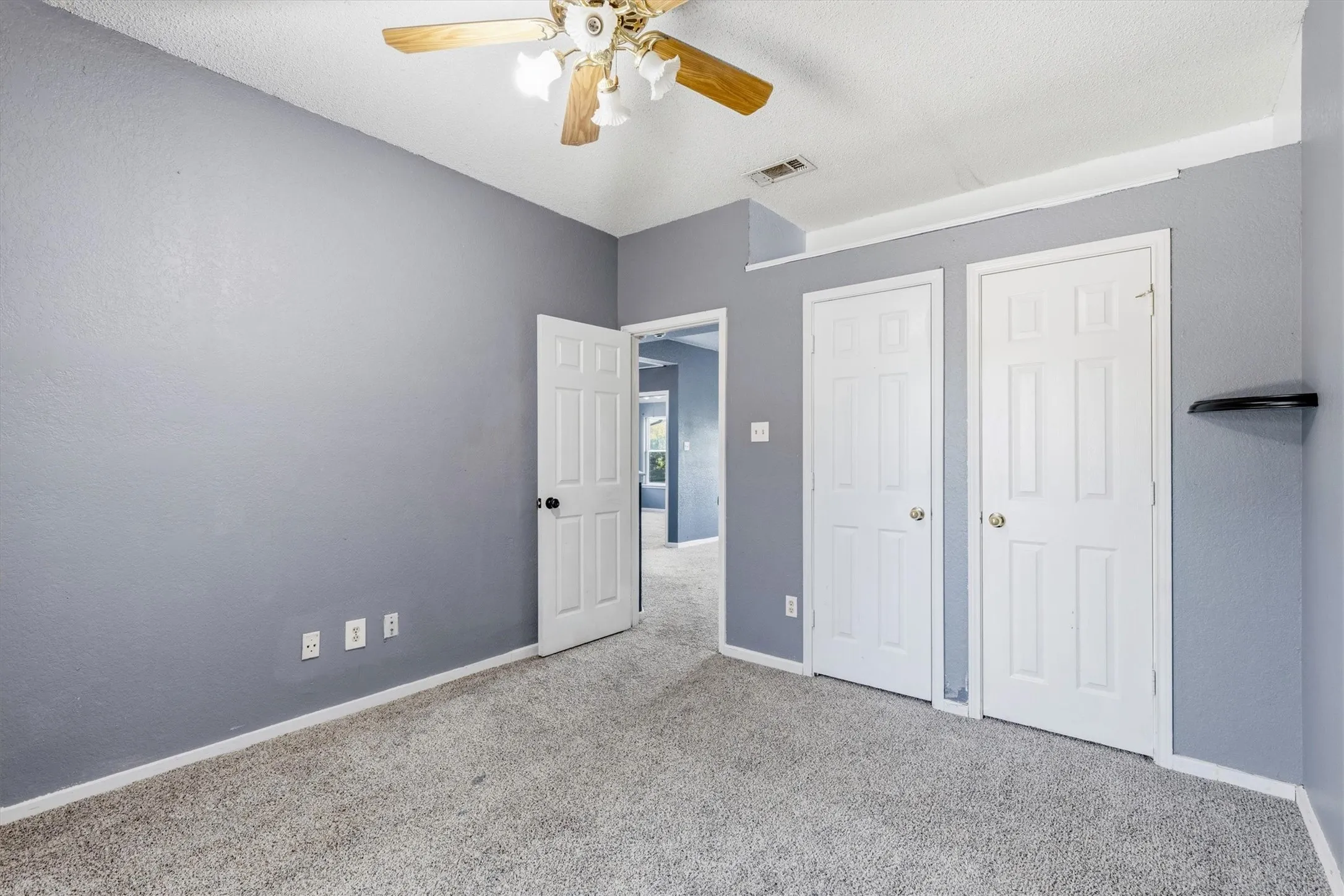 Textured gray walls, light gray carpet flooring, white paneled doors, and a ceiling fan with light fixture