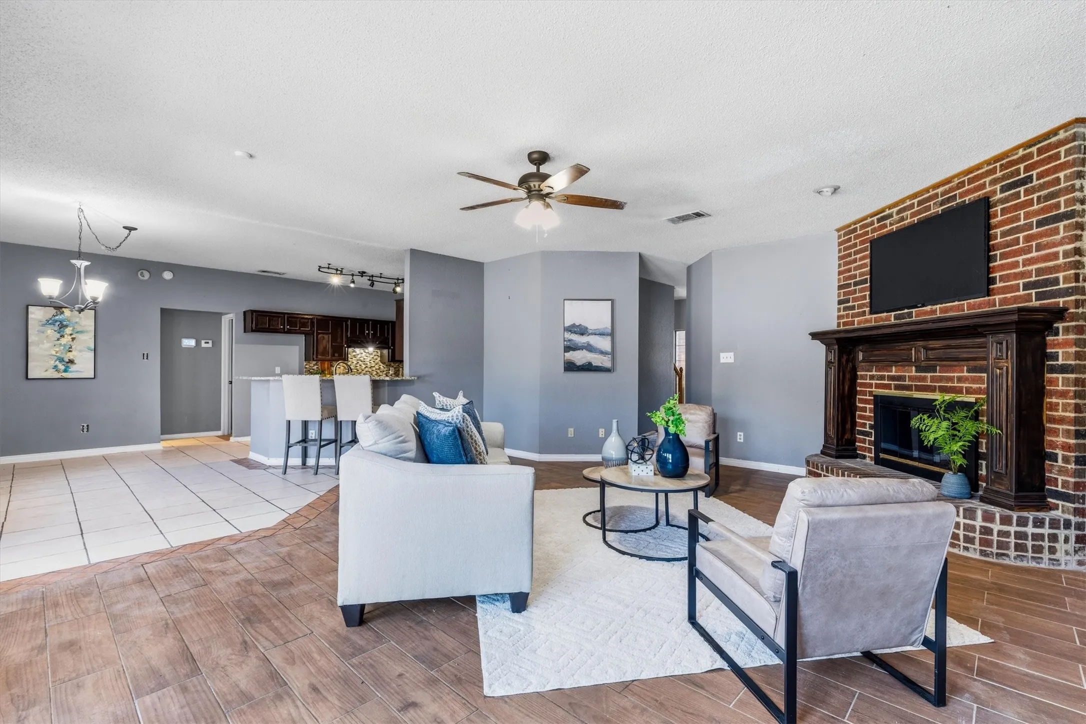 Living area featuring wood-finish flooring, a ceiling fan, and a brick fireplace with a wood mantel