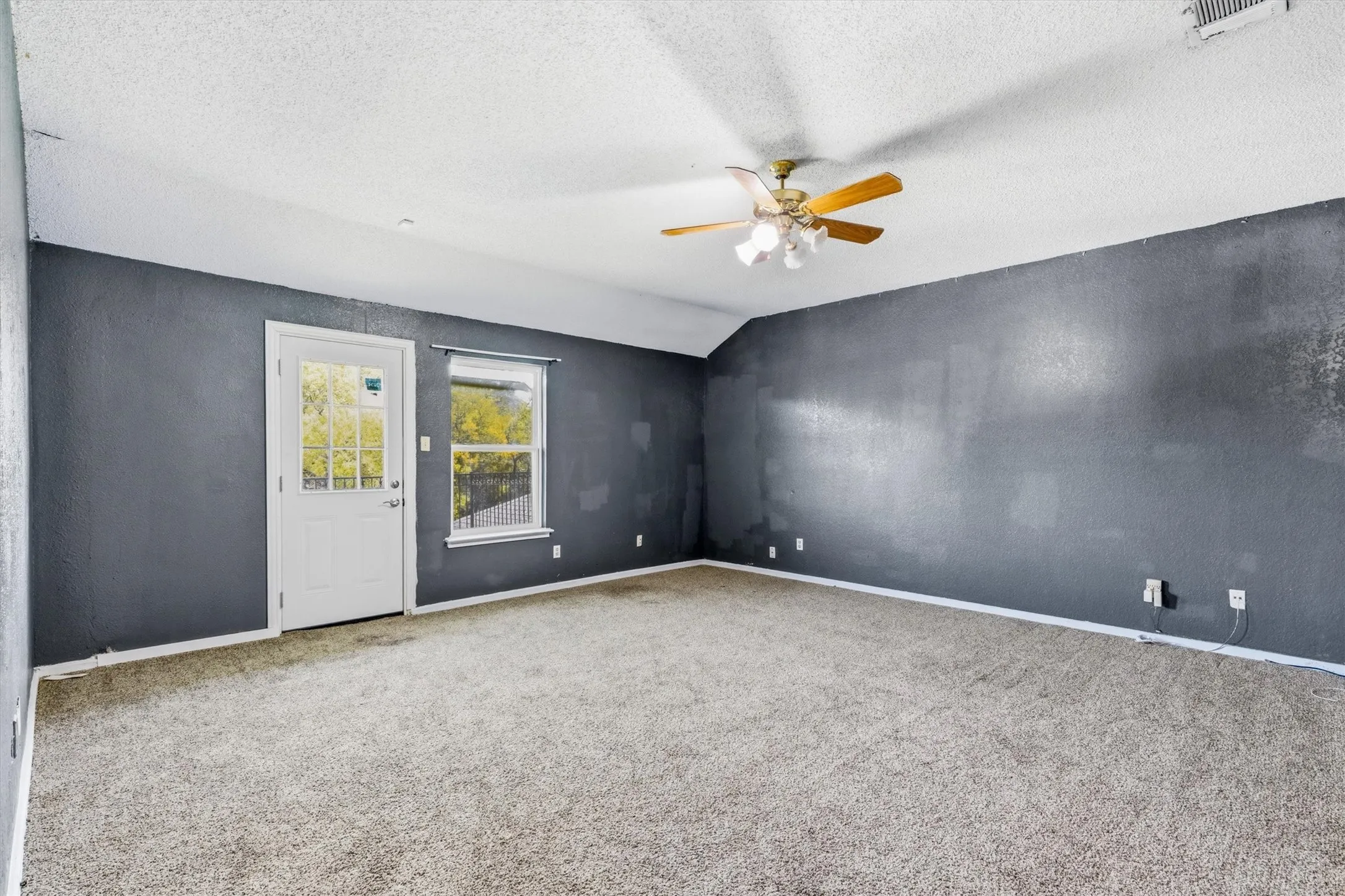 Spacious room featuring neutral carpet flooring, soft white ceiling with ceiling fan, and glass door and window with natural light