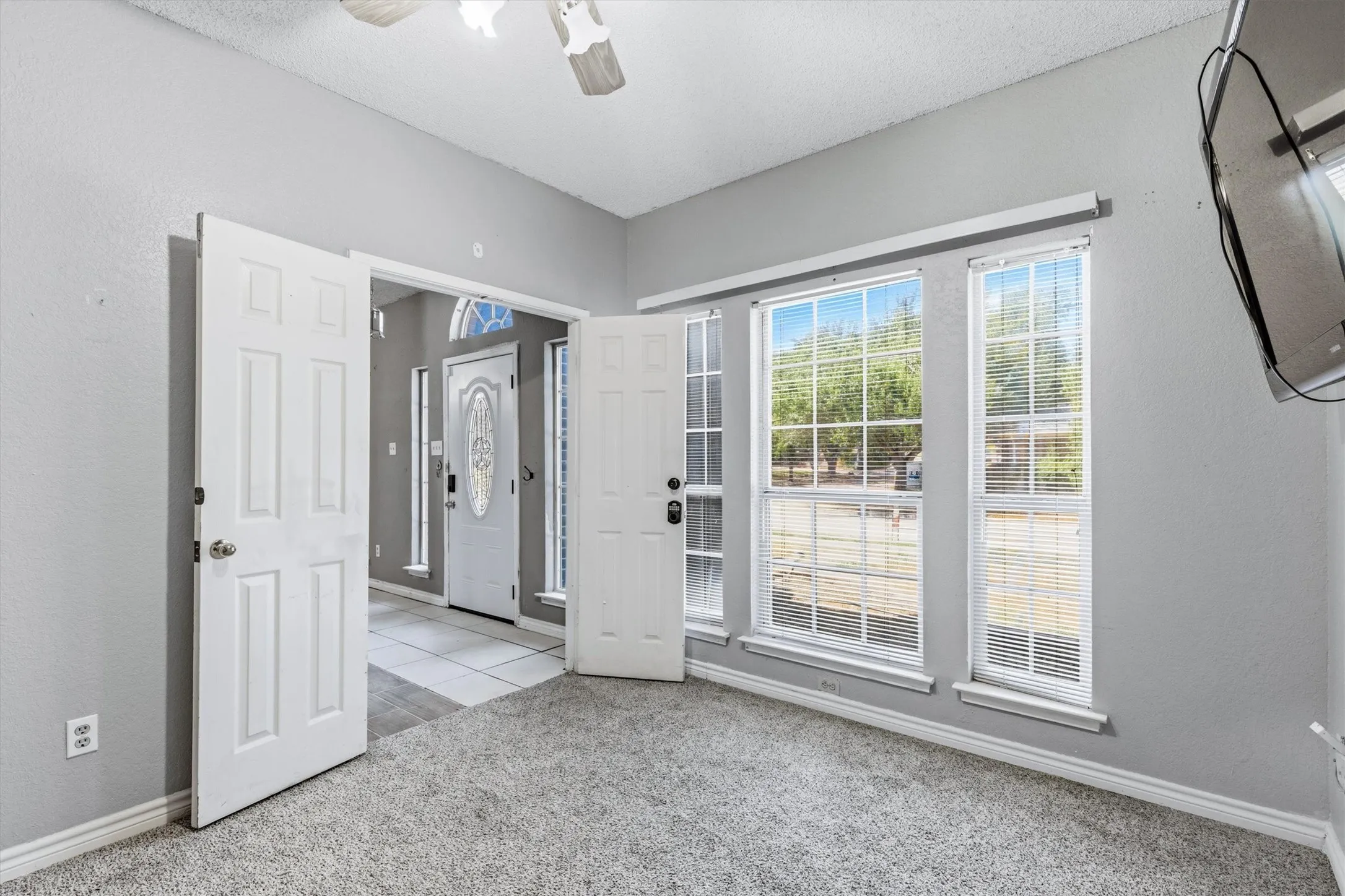 Light gray wall paint, textured ceiling, carpeted flooring, multiple windows with blinds, and a ceiling fan with integrated lighting