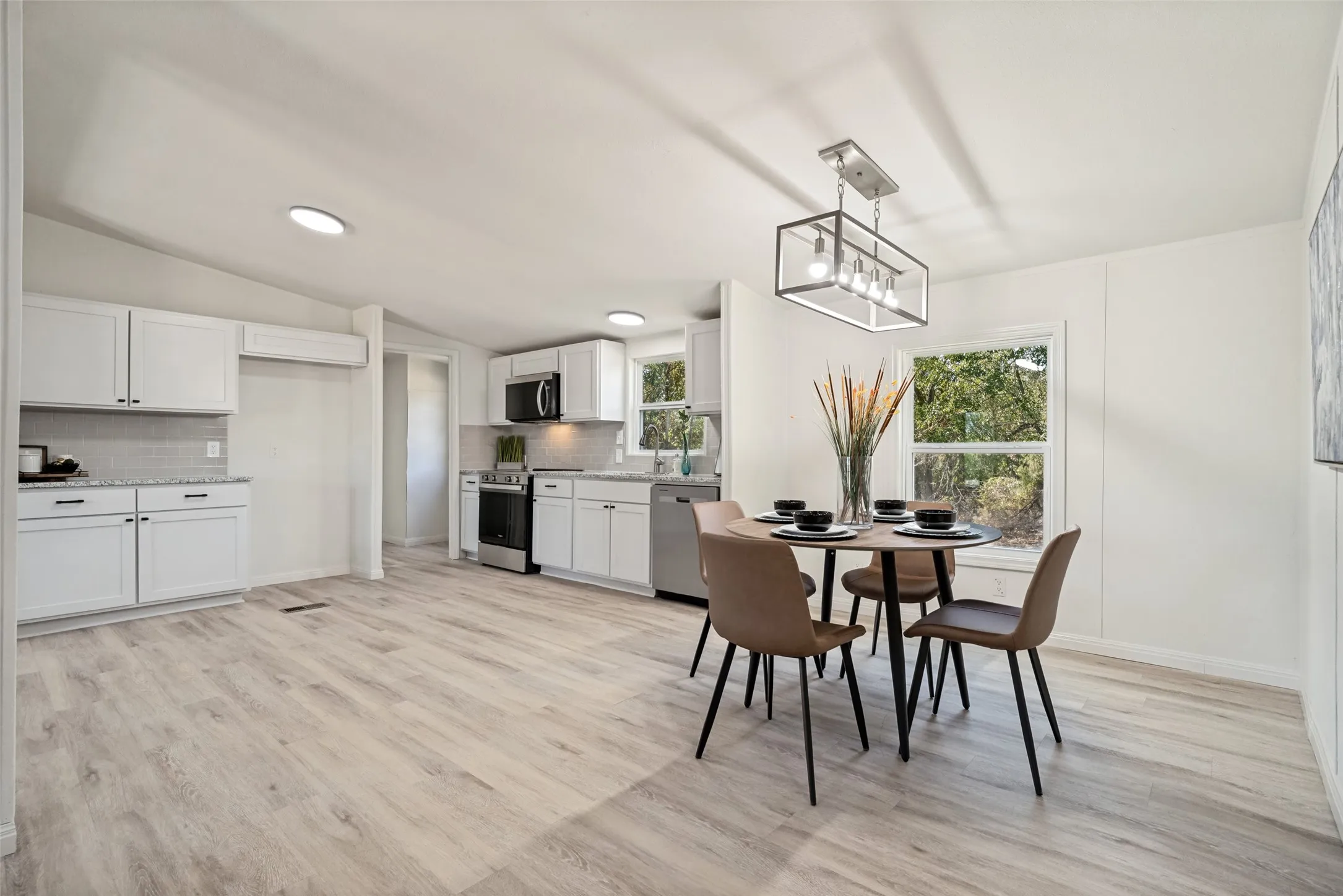 Open-concept kitchen and dining area featuring light wood-finish flooring, white cabinetry, and stainless steel appliances