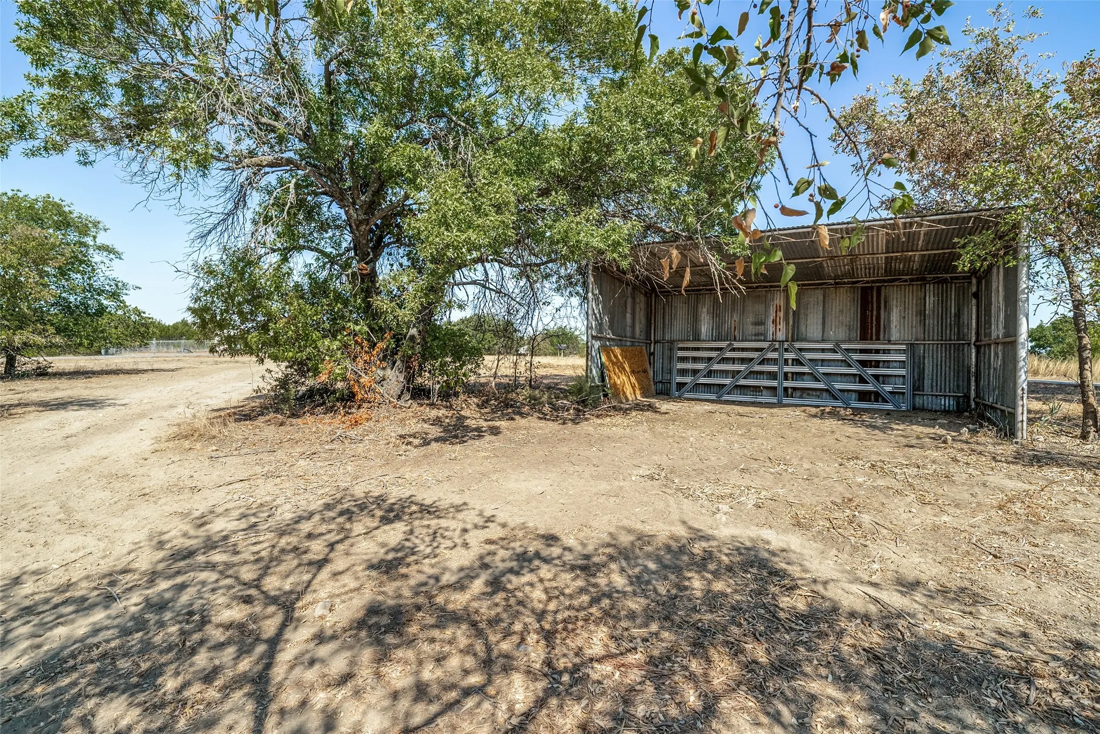 Open-sided shed structure with a corrugated metal roof and walls, featuring a wooden gate