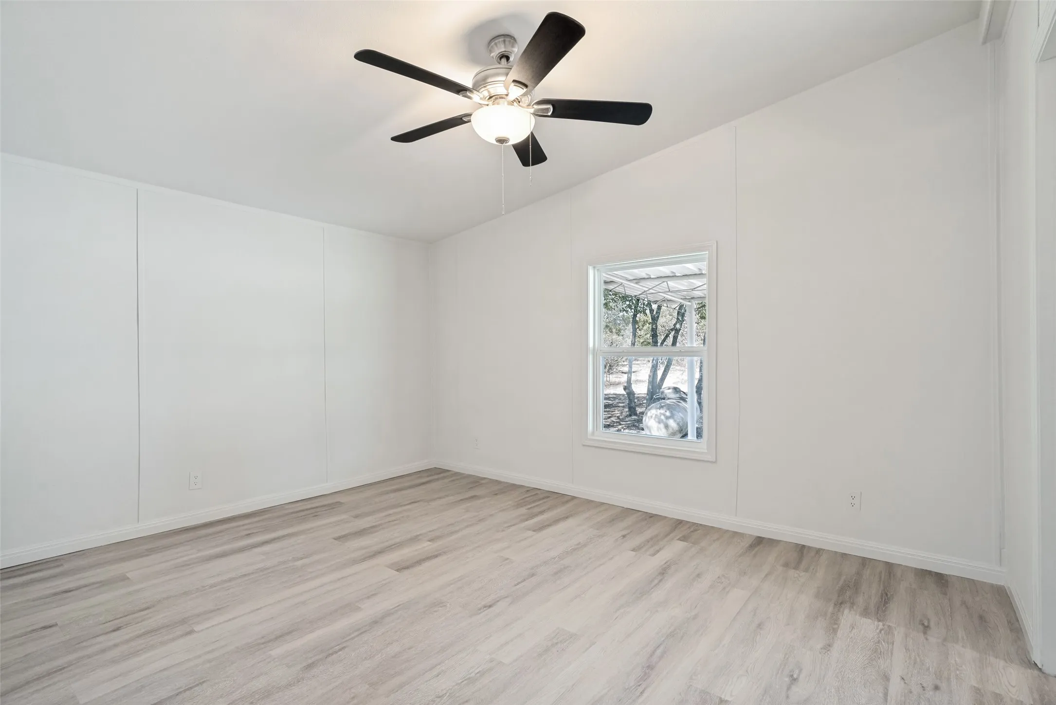 White paneled walls, wood-finish flooring, ceiling fan with light fixture, and a single window