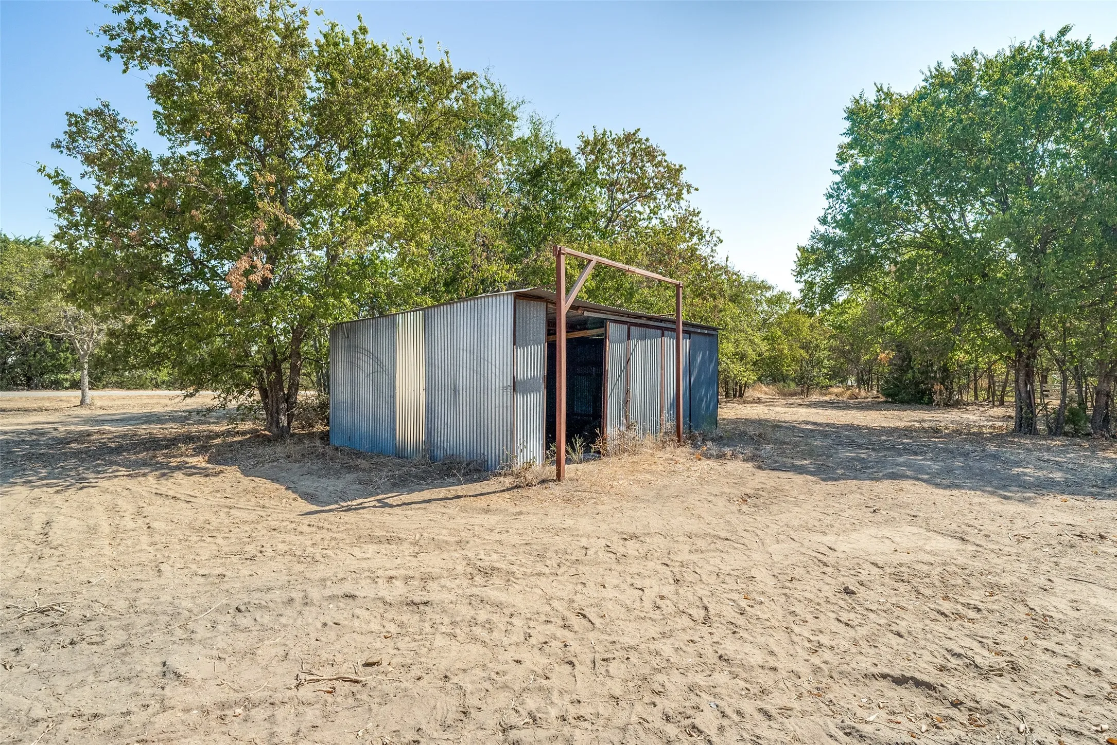 Corrugated metal structure with a metal frame entrance, surrounded by mature trees and natural ground cover