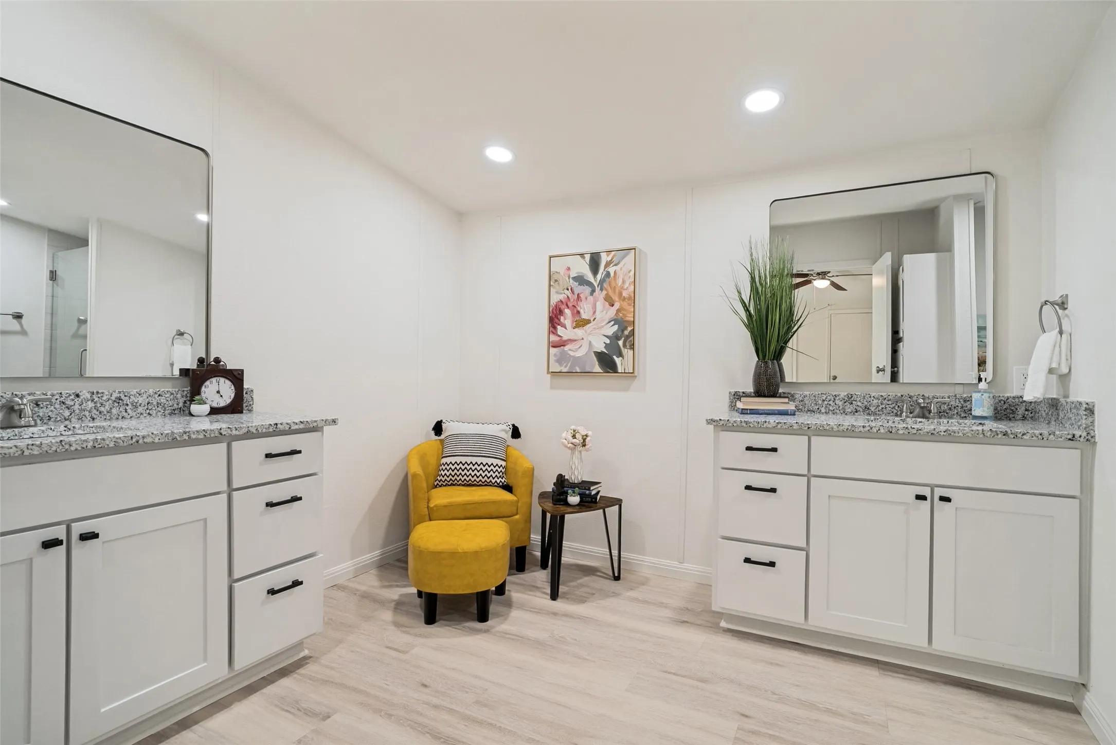 Dual vanity with granite countertops, light wood-finish flooring, recessed ceiling lighting, and panel walls