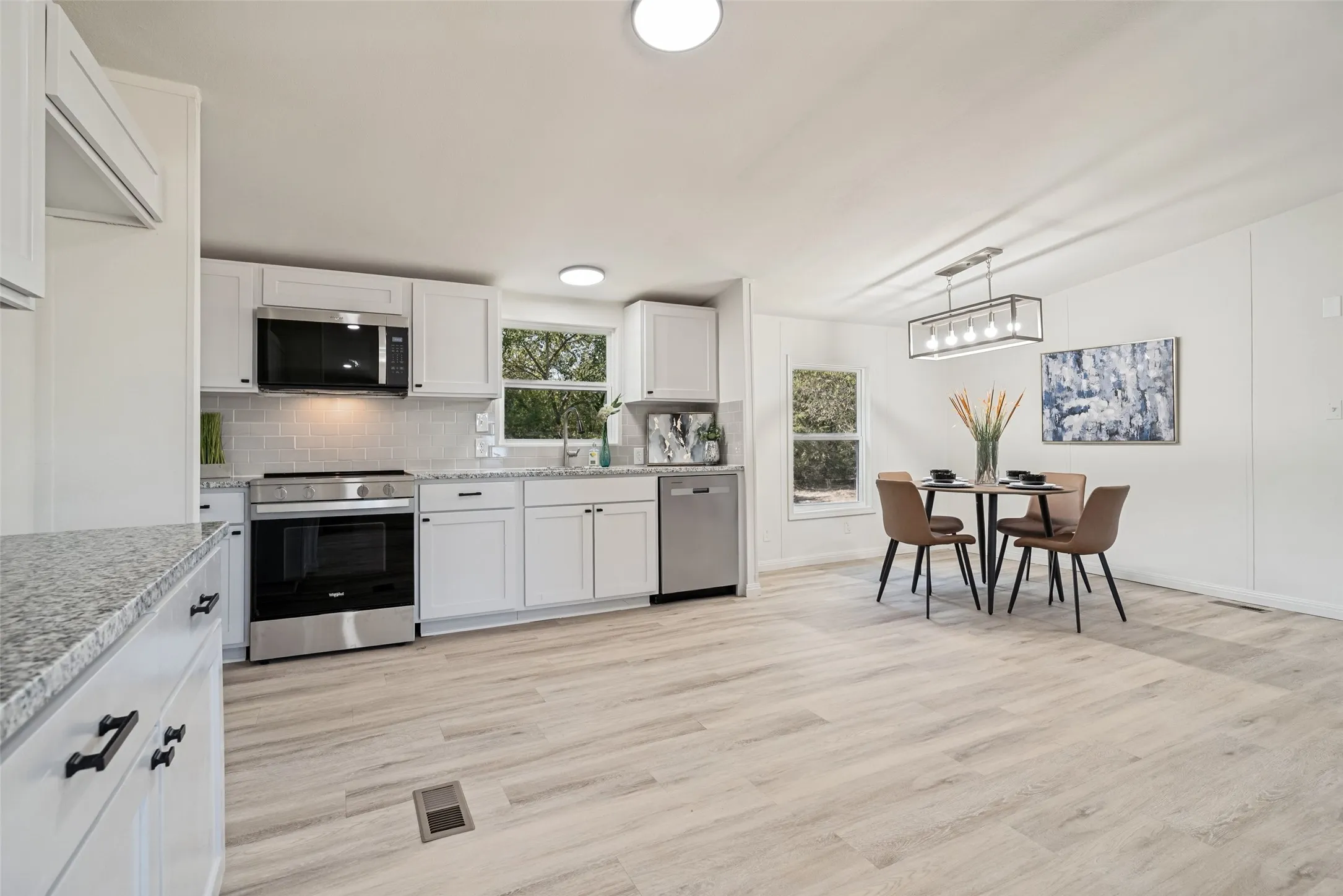Kitchen featuring white cabinetry, stainless steel appliances, speckled countertops, and wood-finish flooring