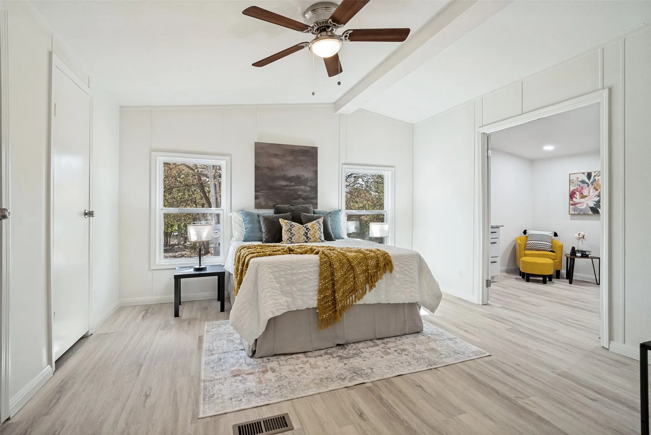 Wood-finish flooring throughout, bright white walls, two windows, and a ceiling fan with integrated lighting