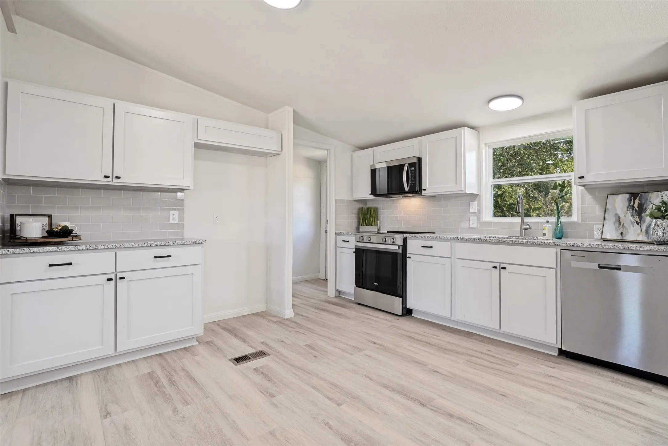 White shaker-style cabinetry, stainless steel appliances, light-toned wood-finish flooring, subway tile backsplash, and stone-look countertops