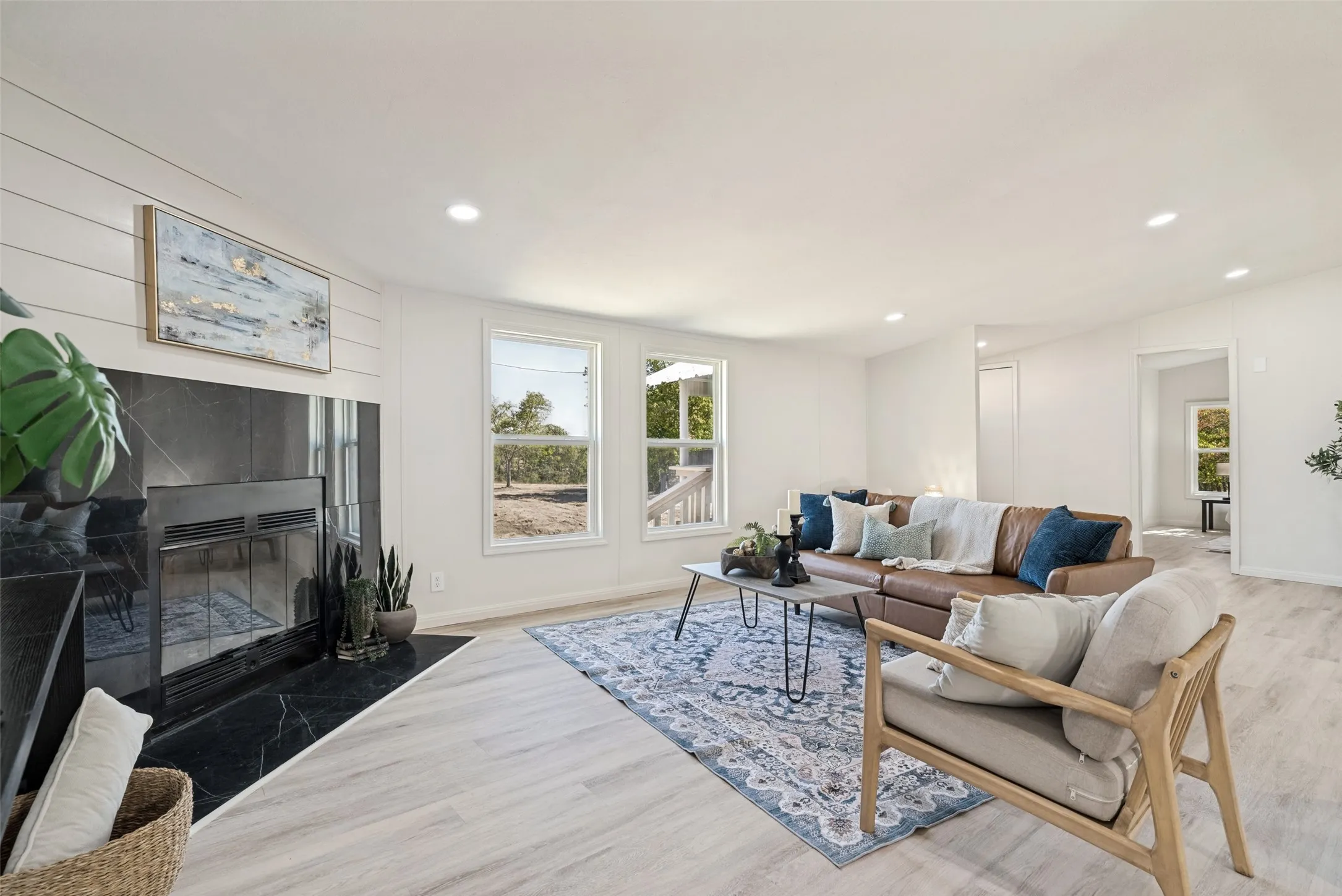 Spacious living area featuring a fireplace with a dark stone surround, wood-finish flooring, recessed lighting, and multiple windows