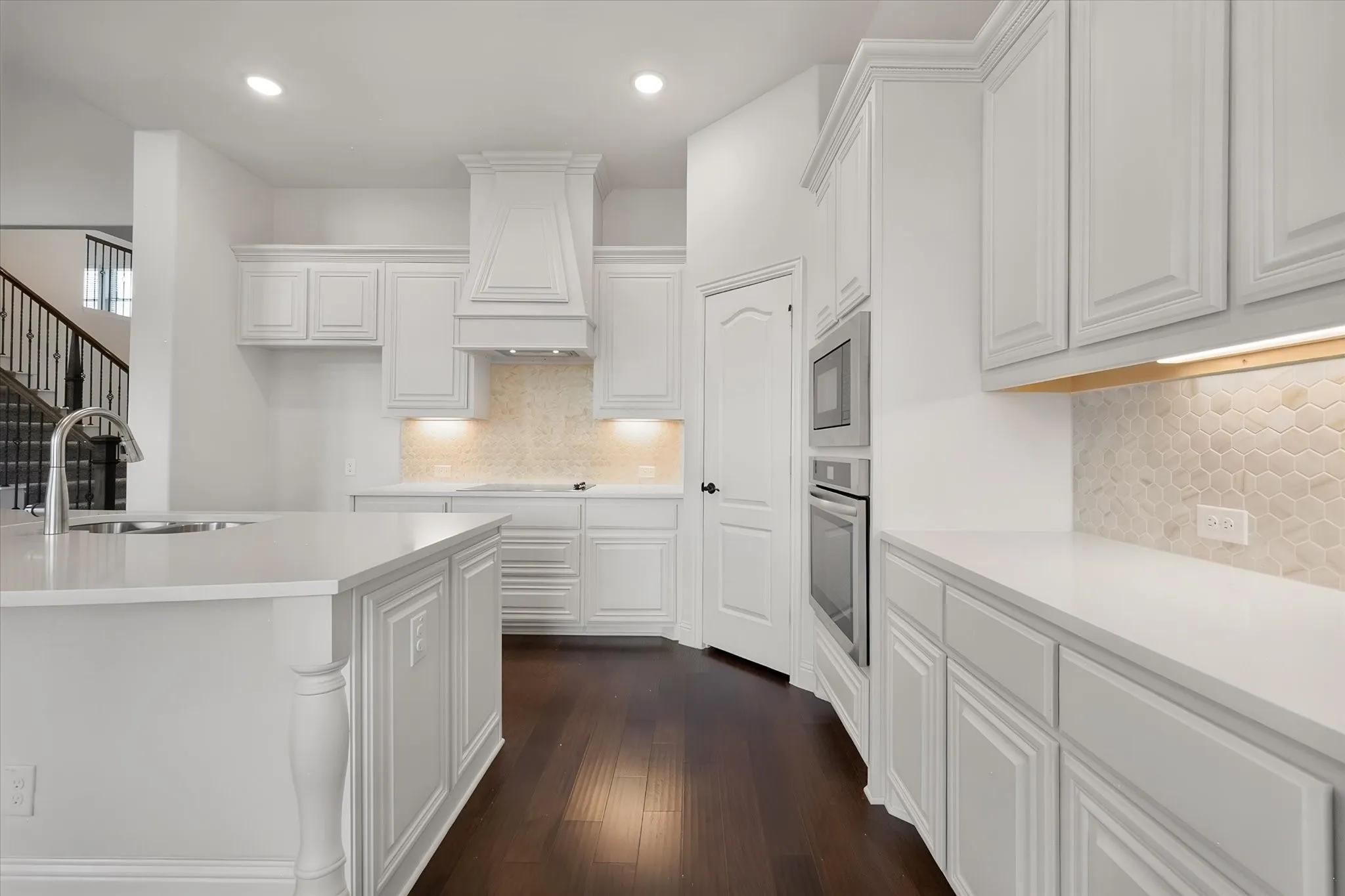This angle shows off the full run of cabinetry — the vent hood, the built-in oven and microwave, and the hexagon tile backsplash adds just the right amount of texture.