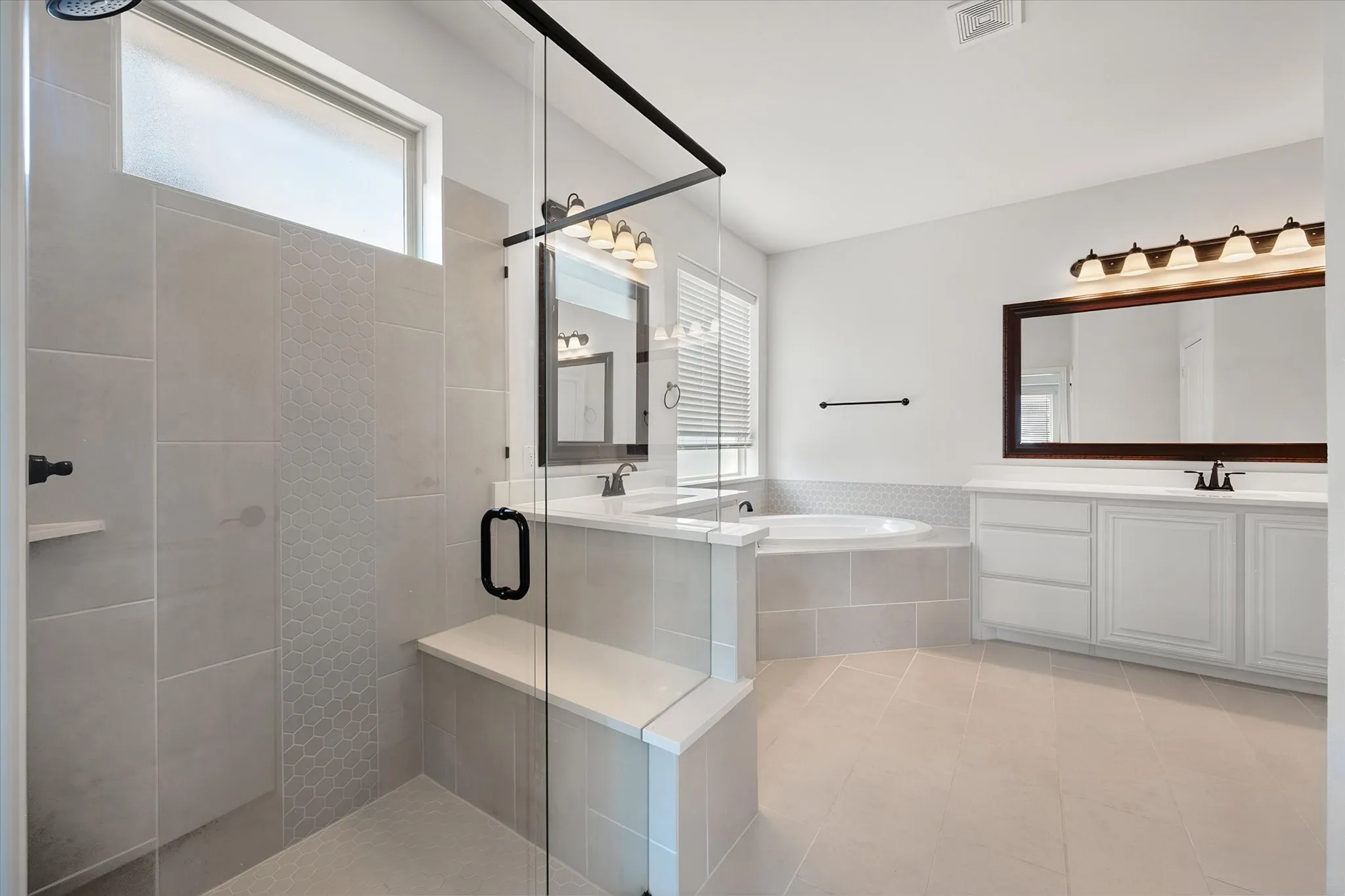 This bathroom is a showstopper — a glass walk-in shower with hexagon tile detail, a deep soaking tub tucked under the window, and dual vanities so you never have to share sink space.