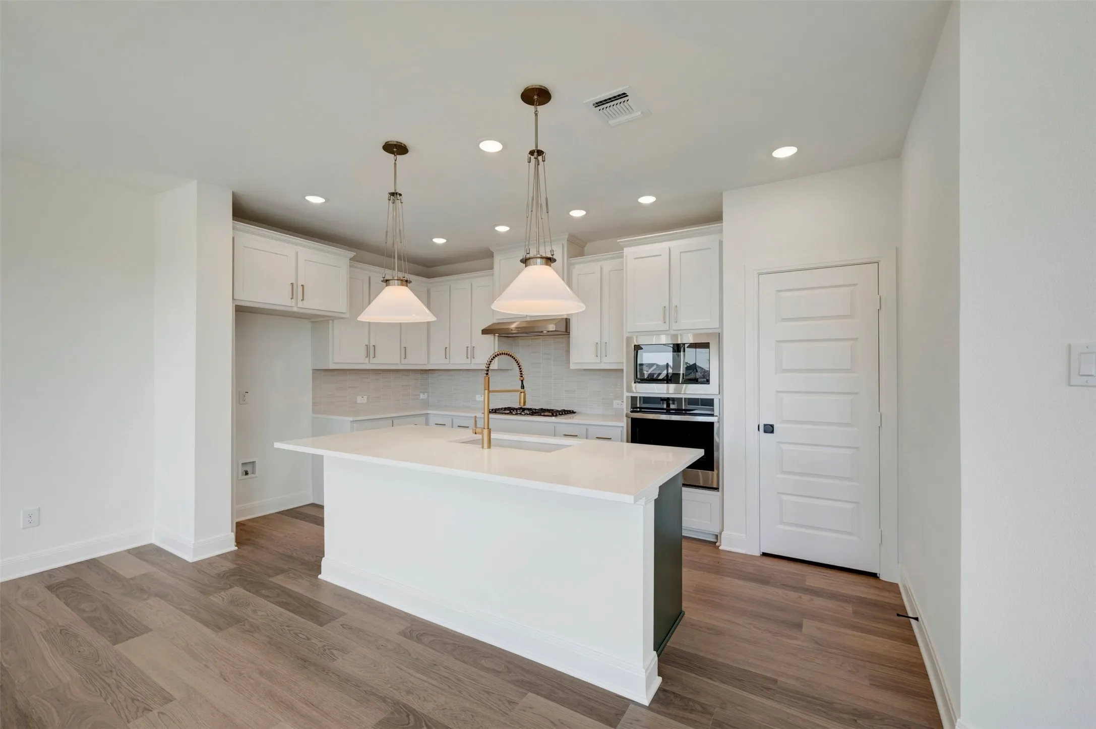 Gourmet kitchen featuring white shaker cabinetry, an island with a light-colored countertop, recessed lighting, and wood-finish flooring