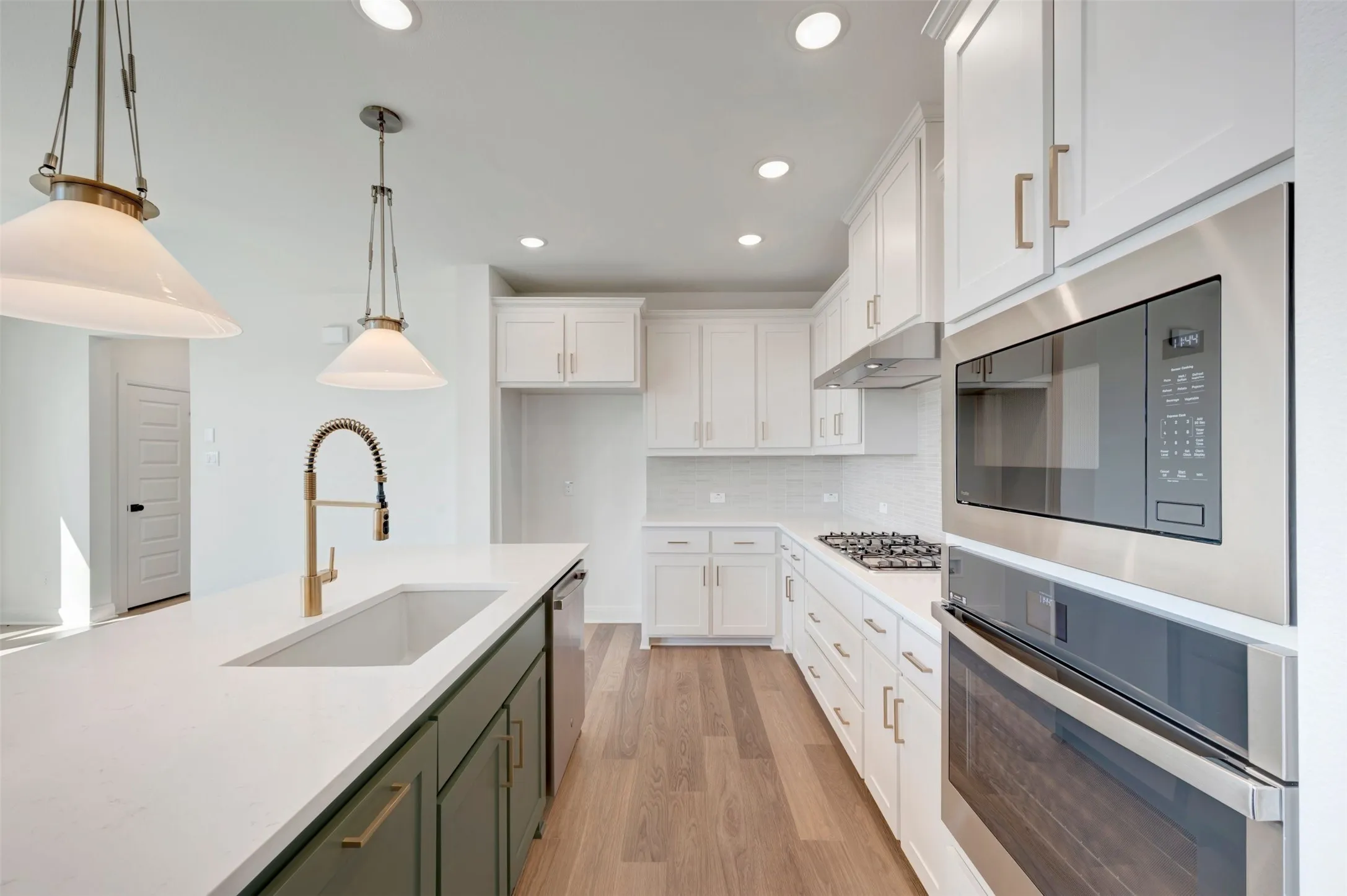 White shaker cabinetry, light wood-finish flooring, stainless steel appliances, recessed lighting, and a kitchen island with an undermount sink