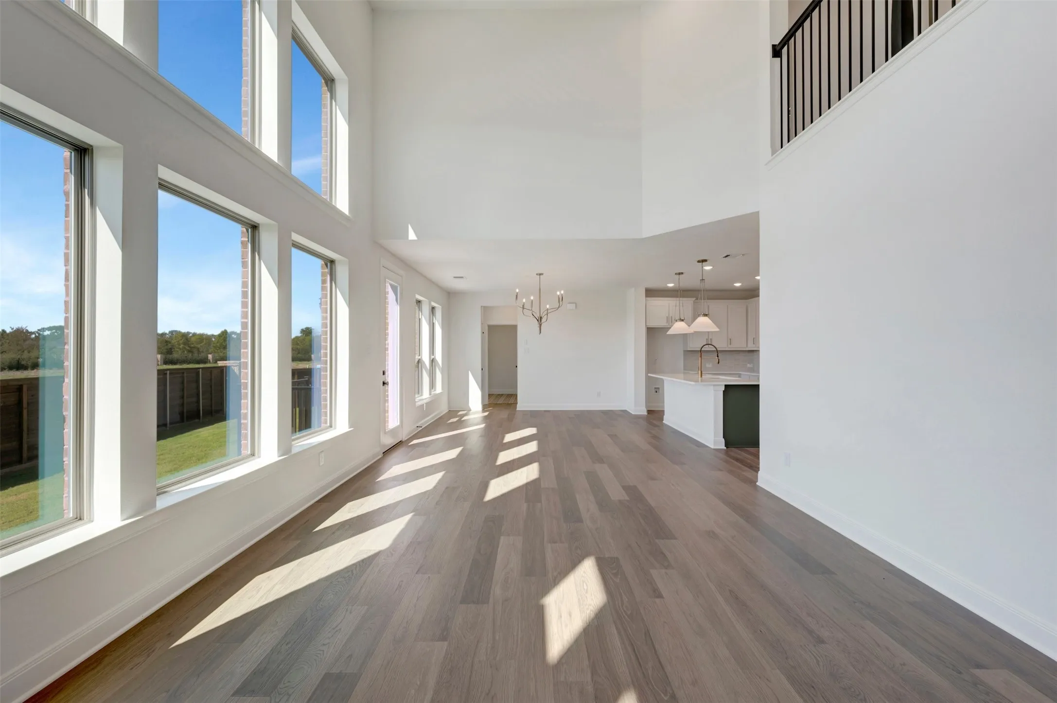 Two-story living area with high ceilings, wood-finish flooring, and multiple large windows