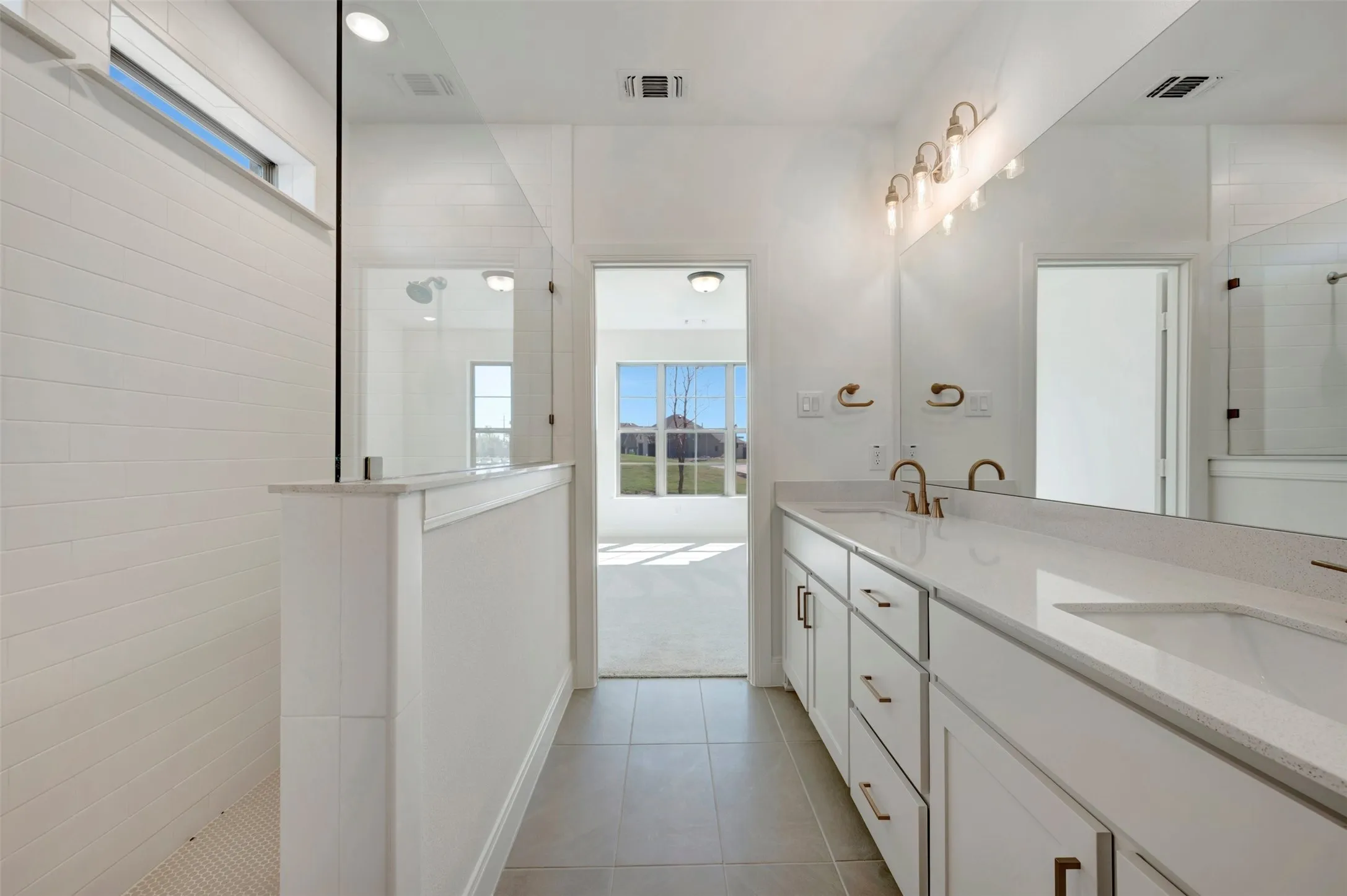 White tile flooring, dual vanities with integrated sinks, white cabinetry, and brushed gold fixtures