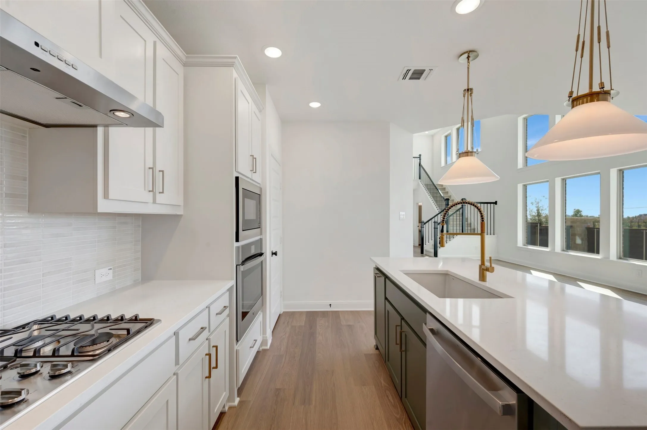 Kitchen featuring white shaker cabinetry, stainless steel appliances, wood-finish flooring, a center island with a sink, and pendant lighting