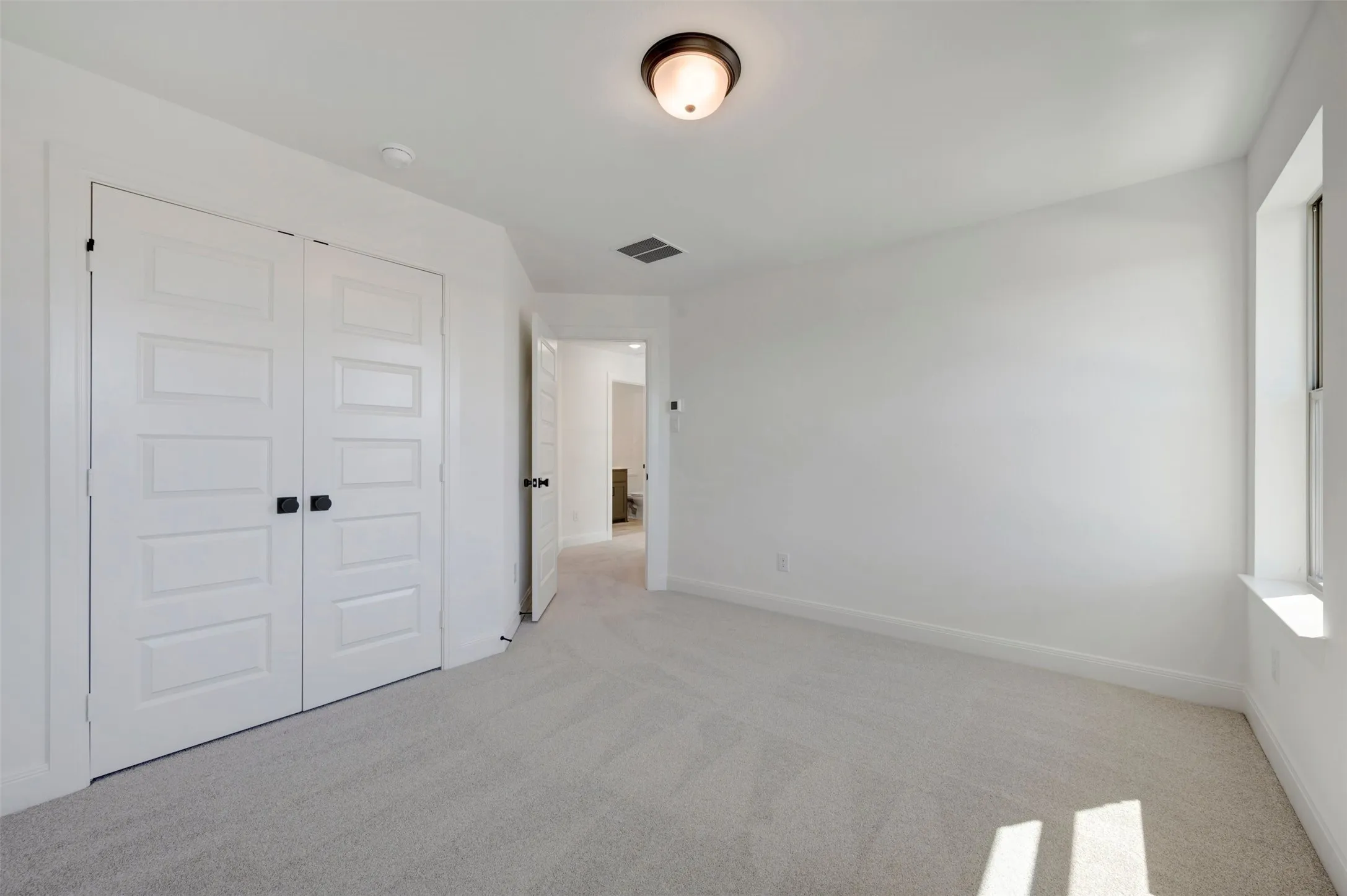 Carpeted flooring, white walls, window with sill, flush mount light fixture, and paneled double doors with dark hardware