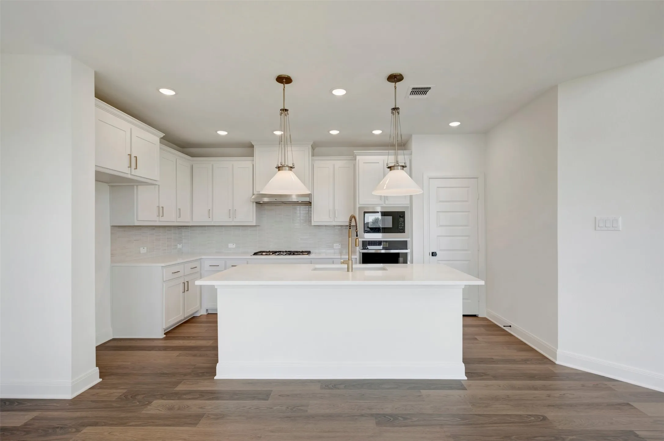 Modern kitchen featuring white shaker cabinetry, an expansive center island, integrated stainless steel appliances, a tile backsplash, and wood-finish flooring