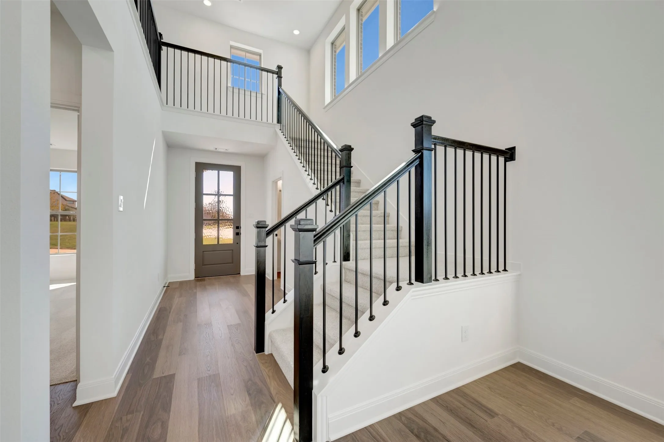 Entryway featuring high ceilings, wood-finish flooring, a contemporary staircase with dark wood newel posts and black metal balusters, and a panel-glass entry door