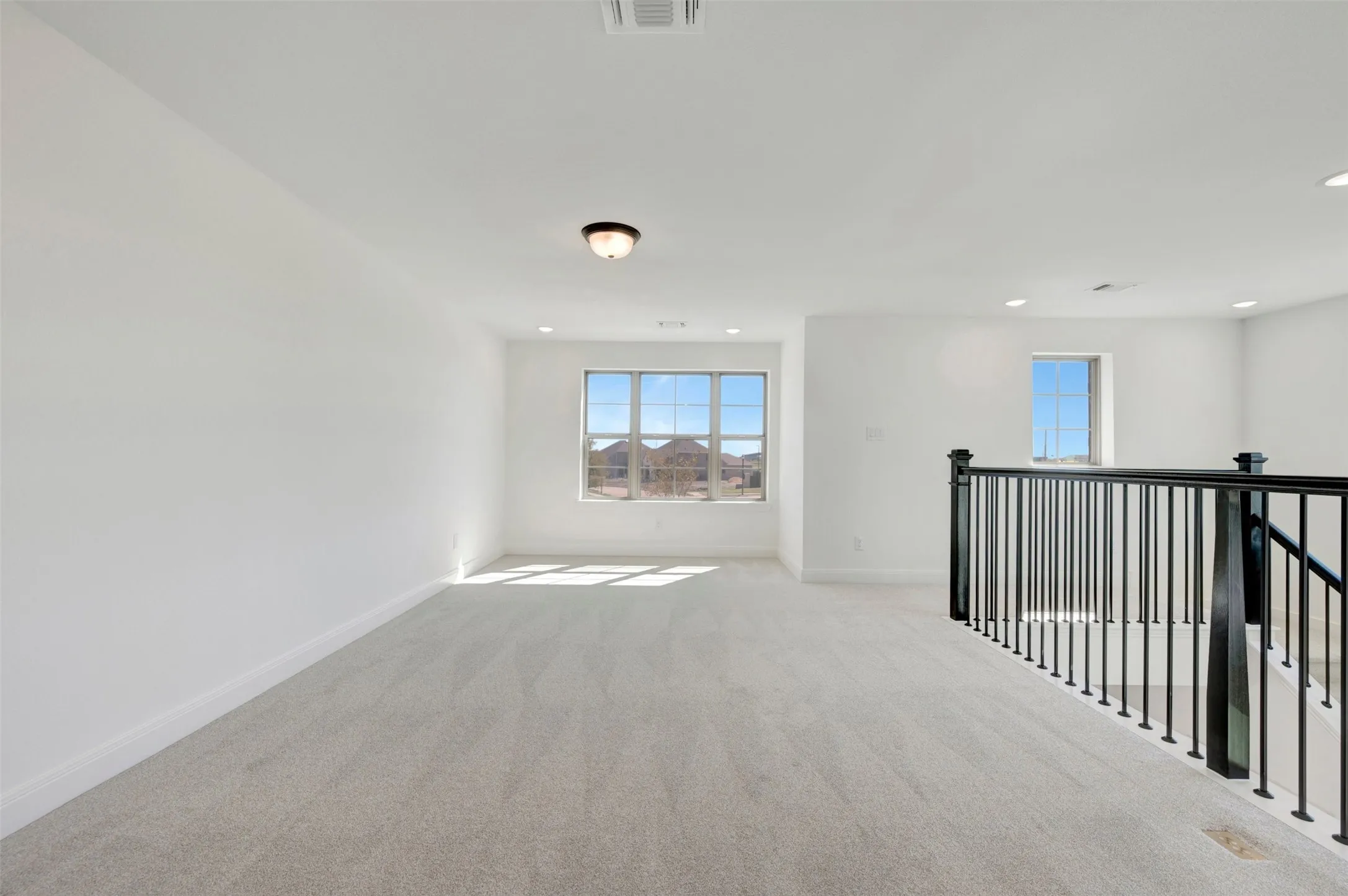 Spacious carpeted area featuring multiple windows, recessed lighting, and a black wrought iron stair railing