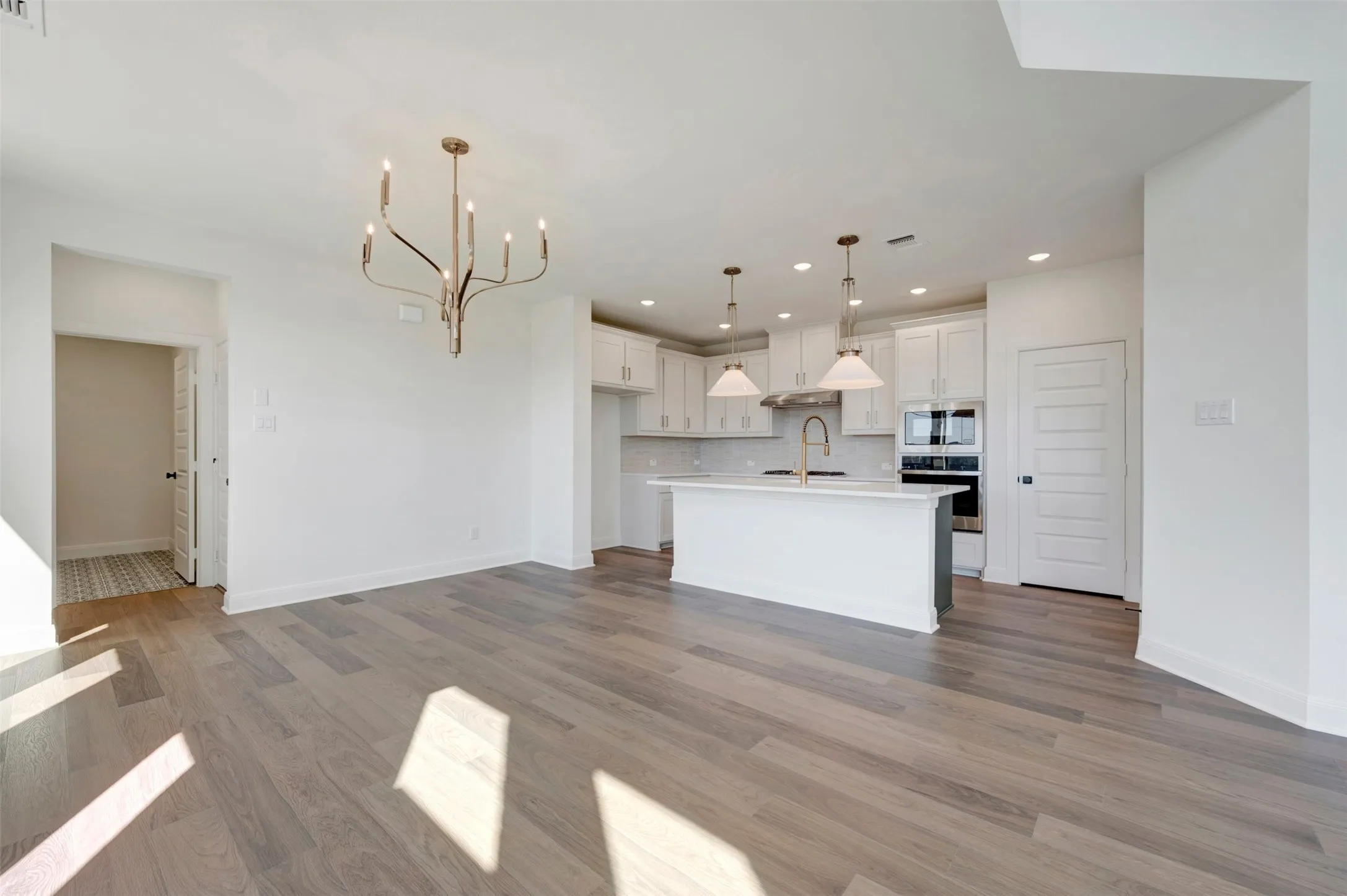 Open-concept living area with wood-finish flooring, a contemporary chandelier, and recessed lighting
