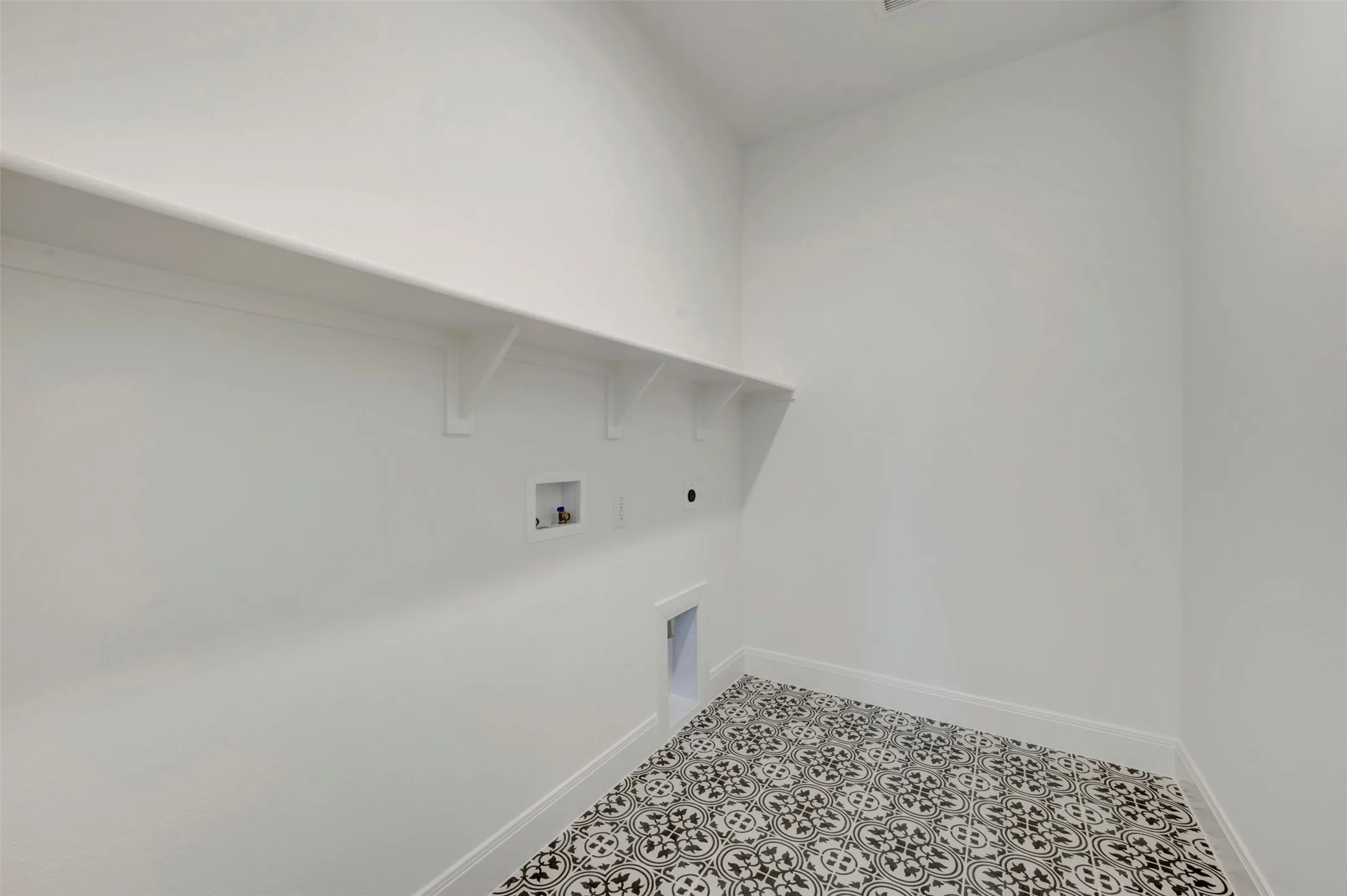 Laundry room featuring a white wall shelf, built-in utility connections, and patterned floor tile