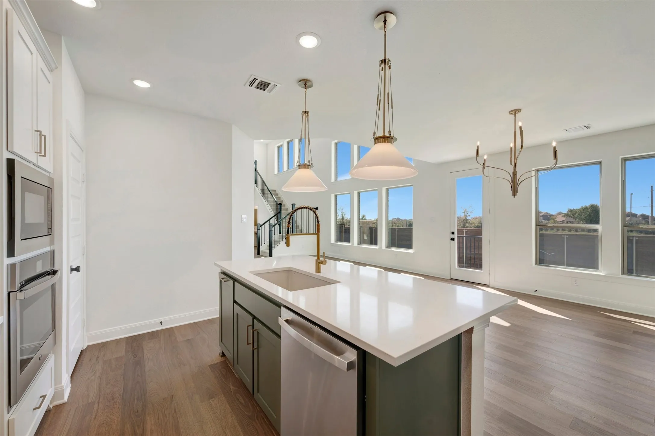 Kitchen with a central island featuring a sink and dishwasher, built-in double ovens, wood-finish flooring, and multiple large windows
