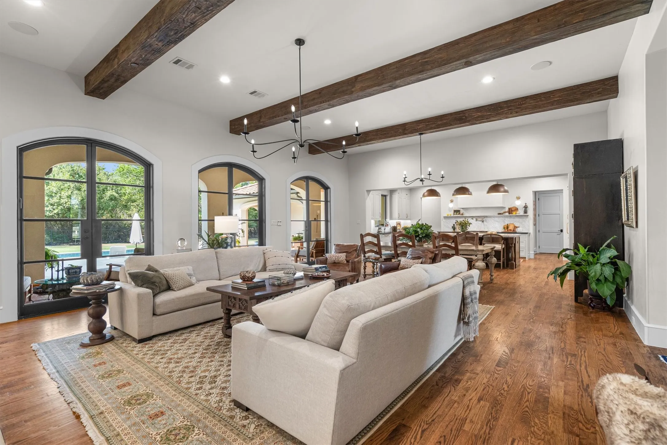 Open-concept living and dining area with exposed wood beam ceilings and walls of windows for natural light.