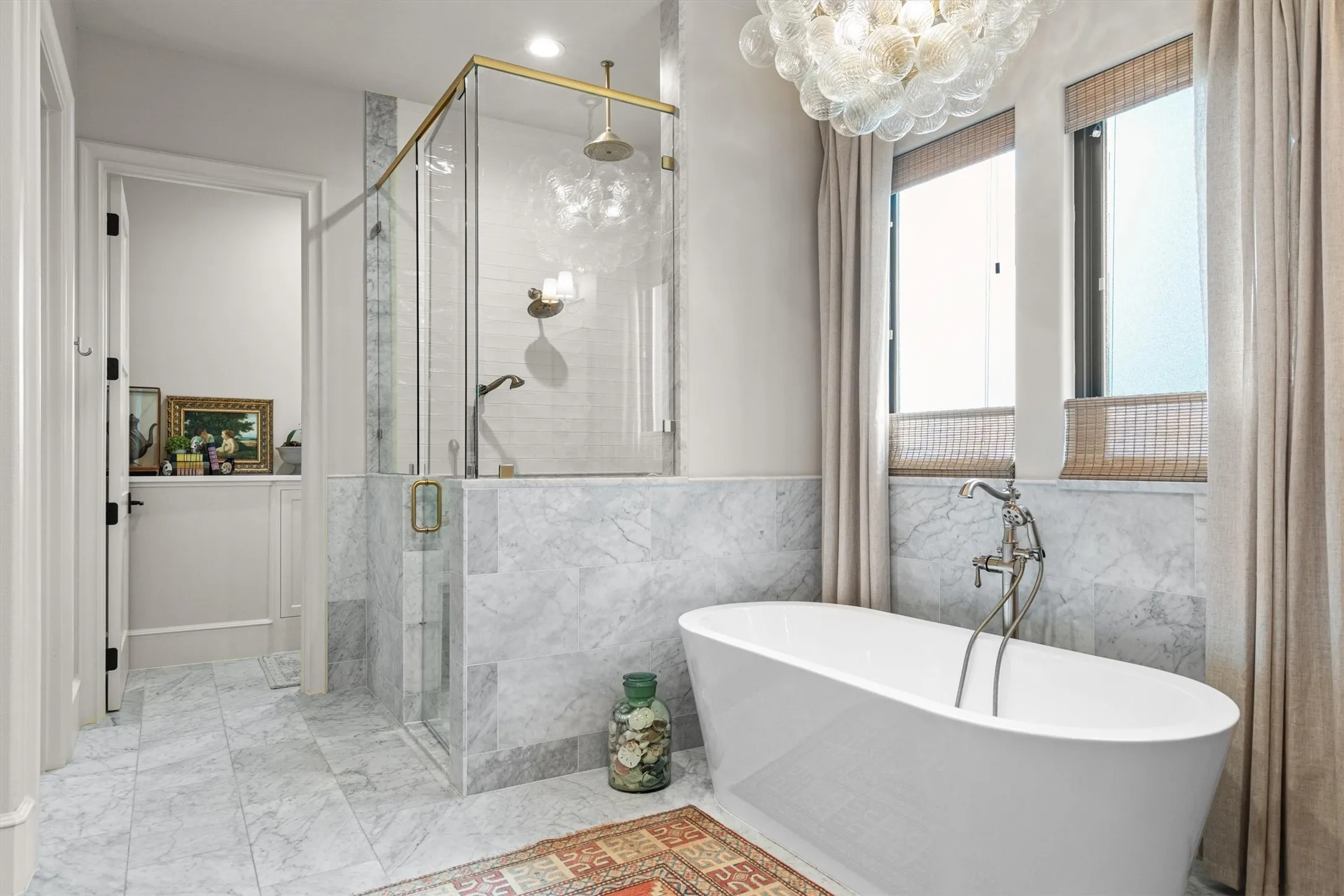 Luxurious primary bath featuring marble-look tile and a statement chandelier.