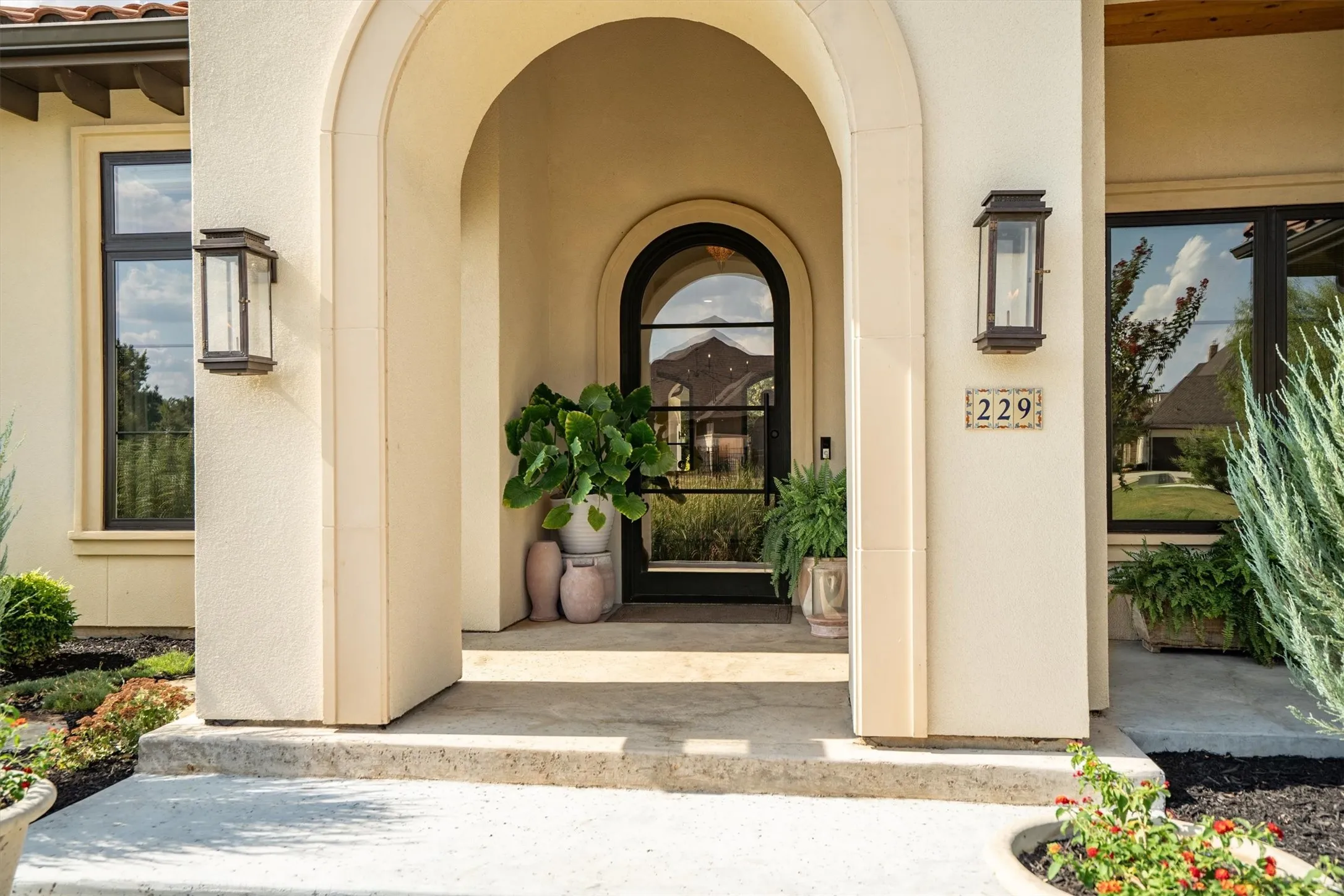 Arched entryway with iron and glass door, stone walkway, and designer lantern sconces welcome you home.