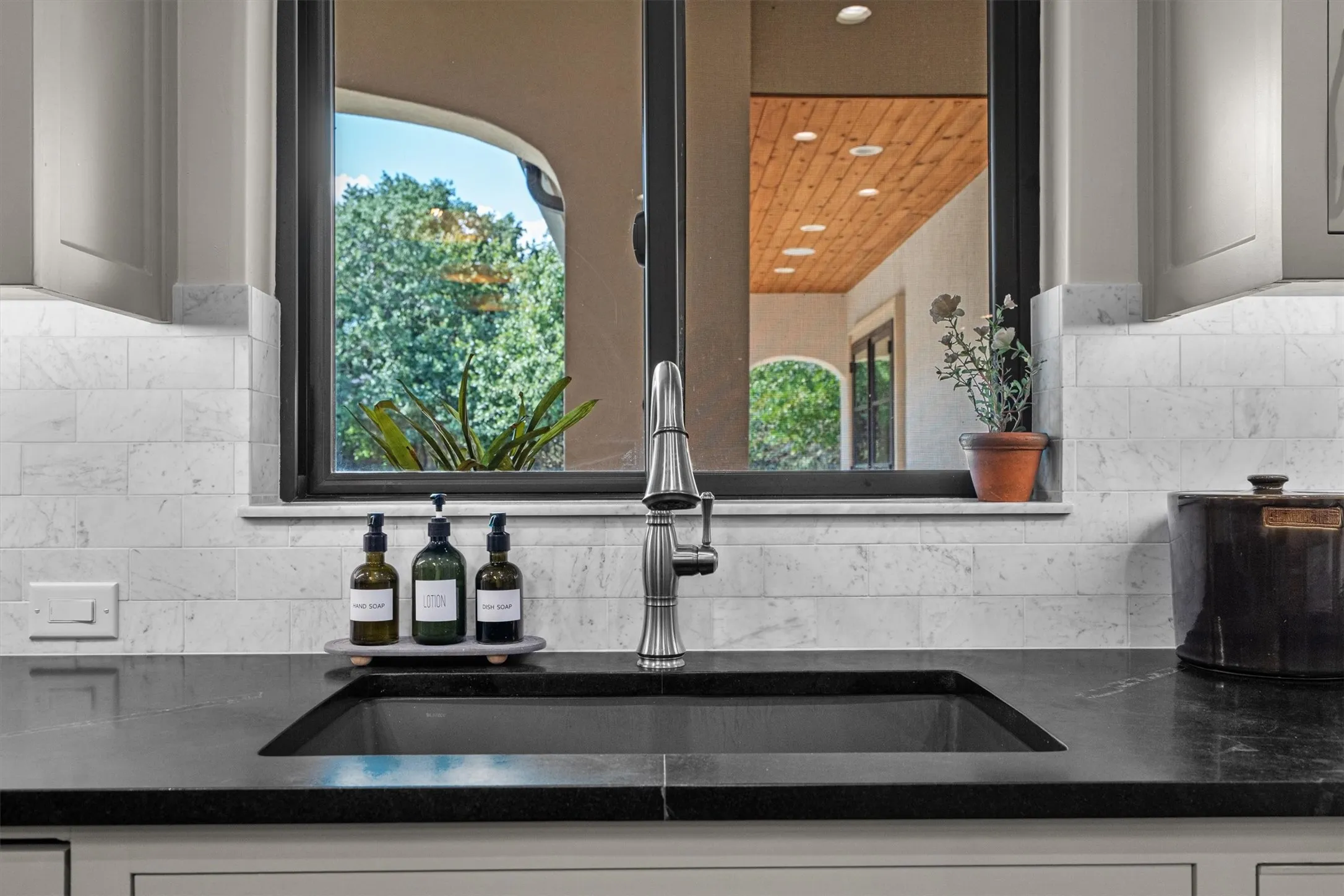 Farmhouse-style prep sink framed by a picture window overlooking mature trees.