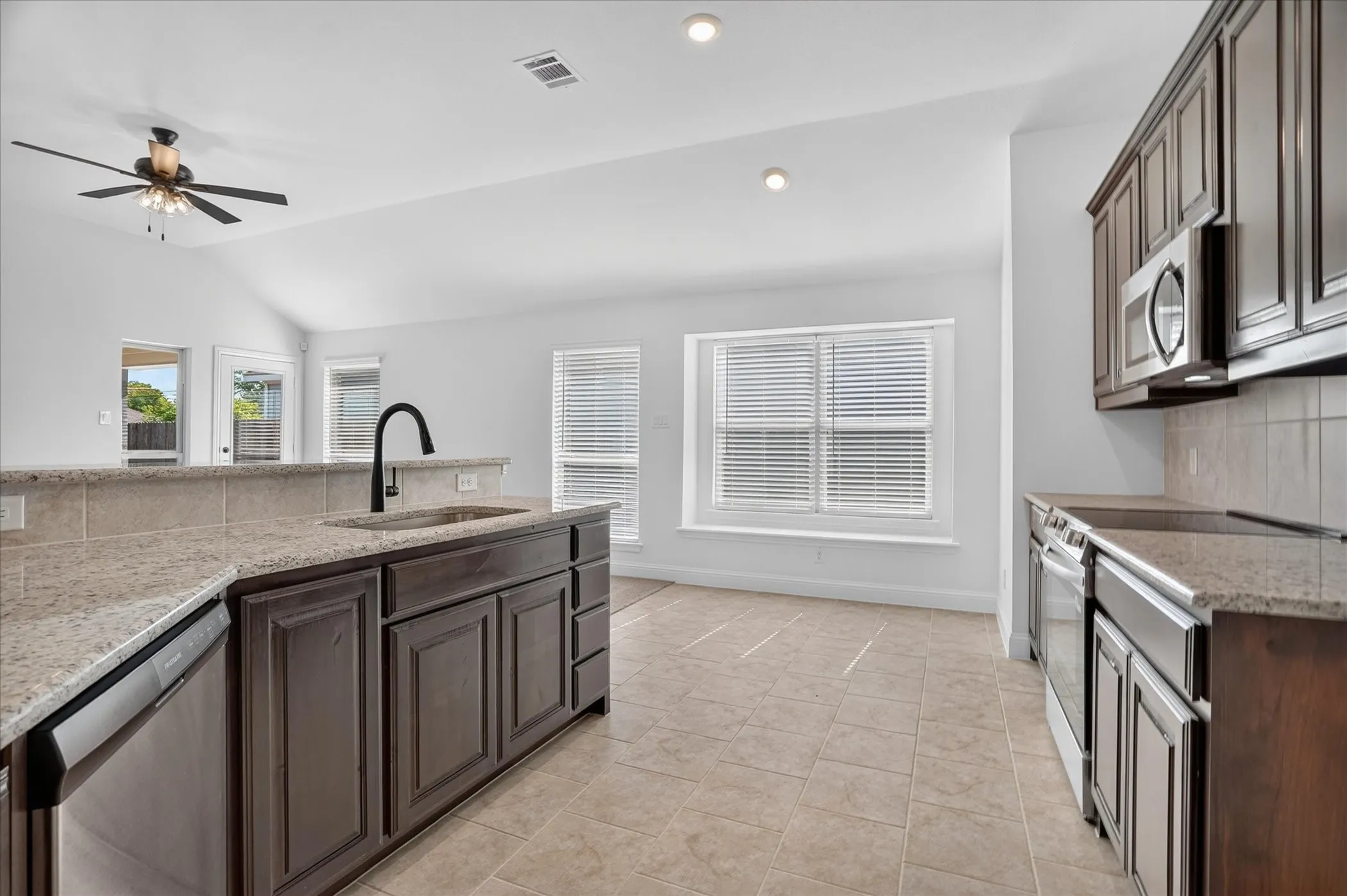 Kitchen featuring dark wood-finish cabinetry, light-toned countertops, stainless steel appliances, and a tile backsplash