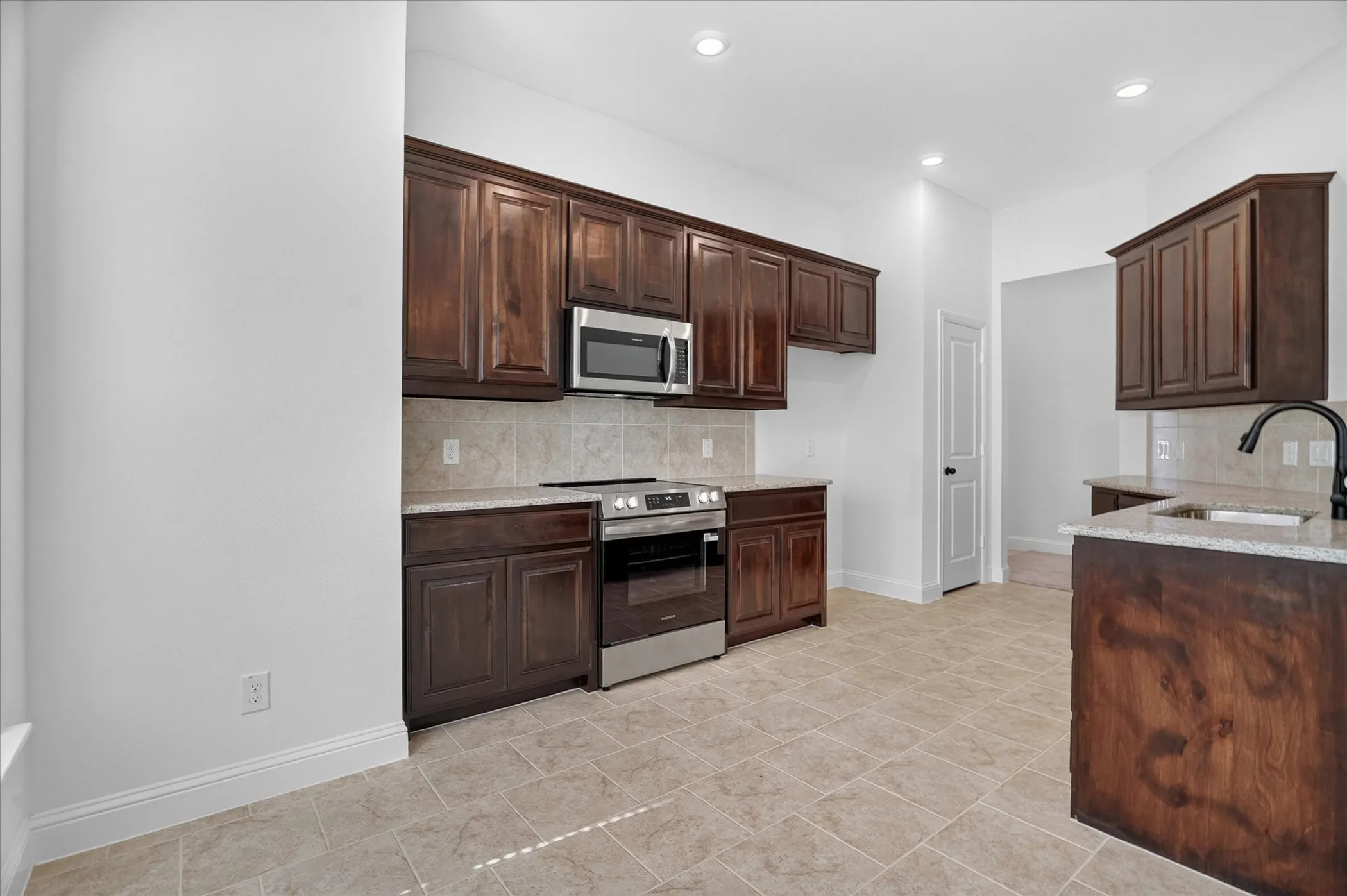 Kitchen with recessed lighting, dark wood-finish cabinetry, stainless steel appliances, light-toned backsplash, and tile flooring
