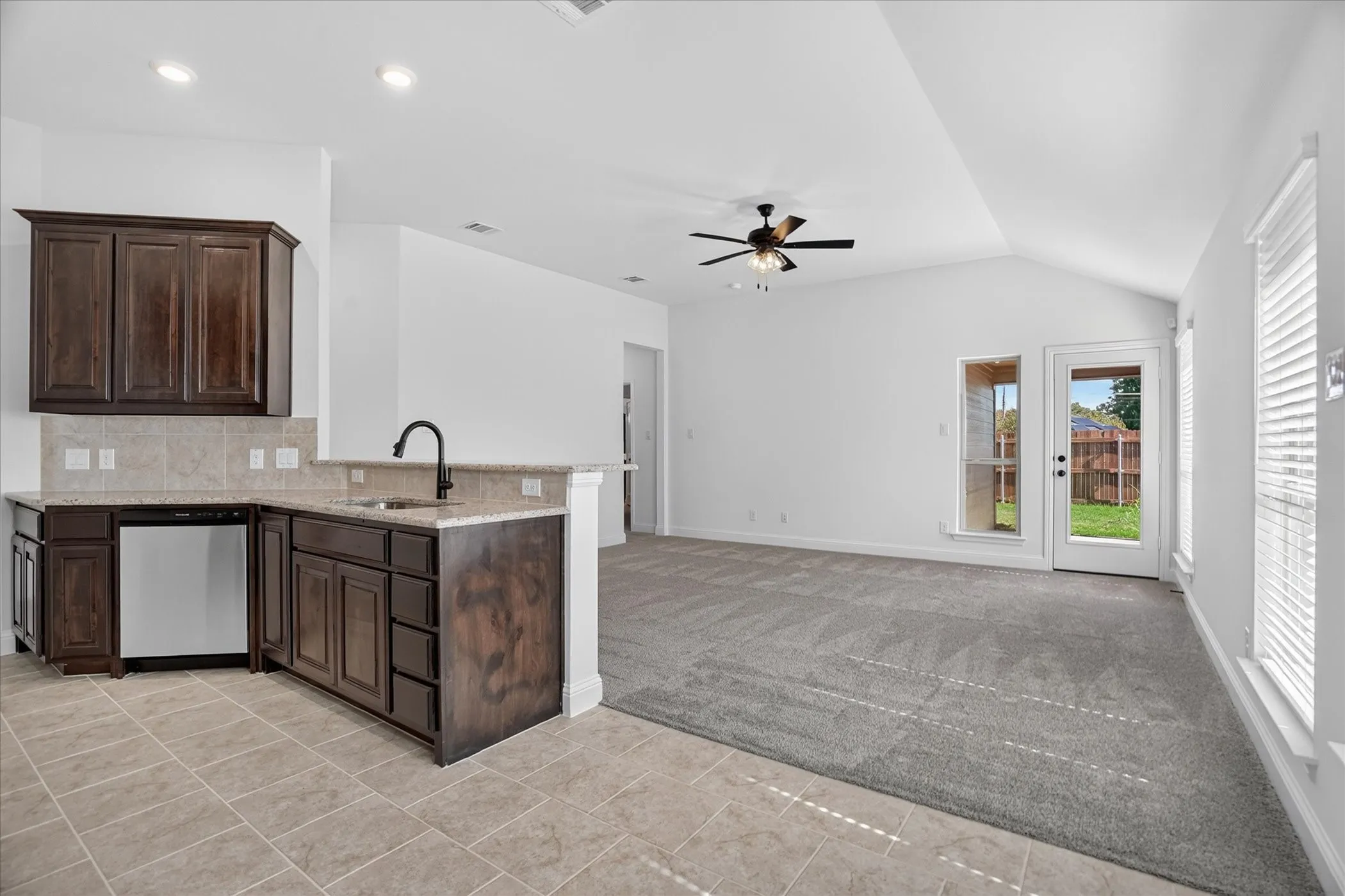 Open-concept living space featuring a kitchen with dark wood-finish cabinetry, a tile backsplash, and a built-in dishwasher