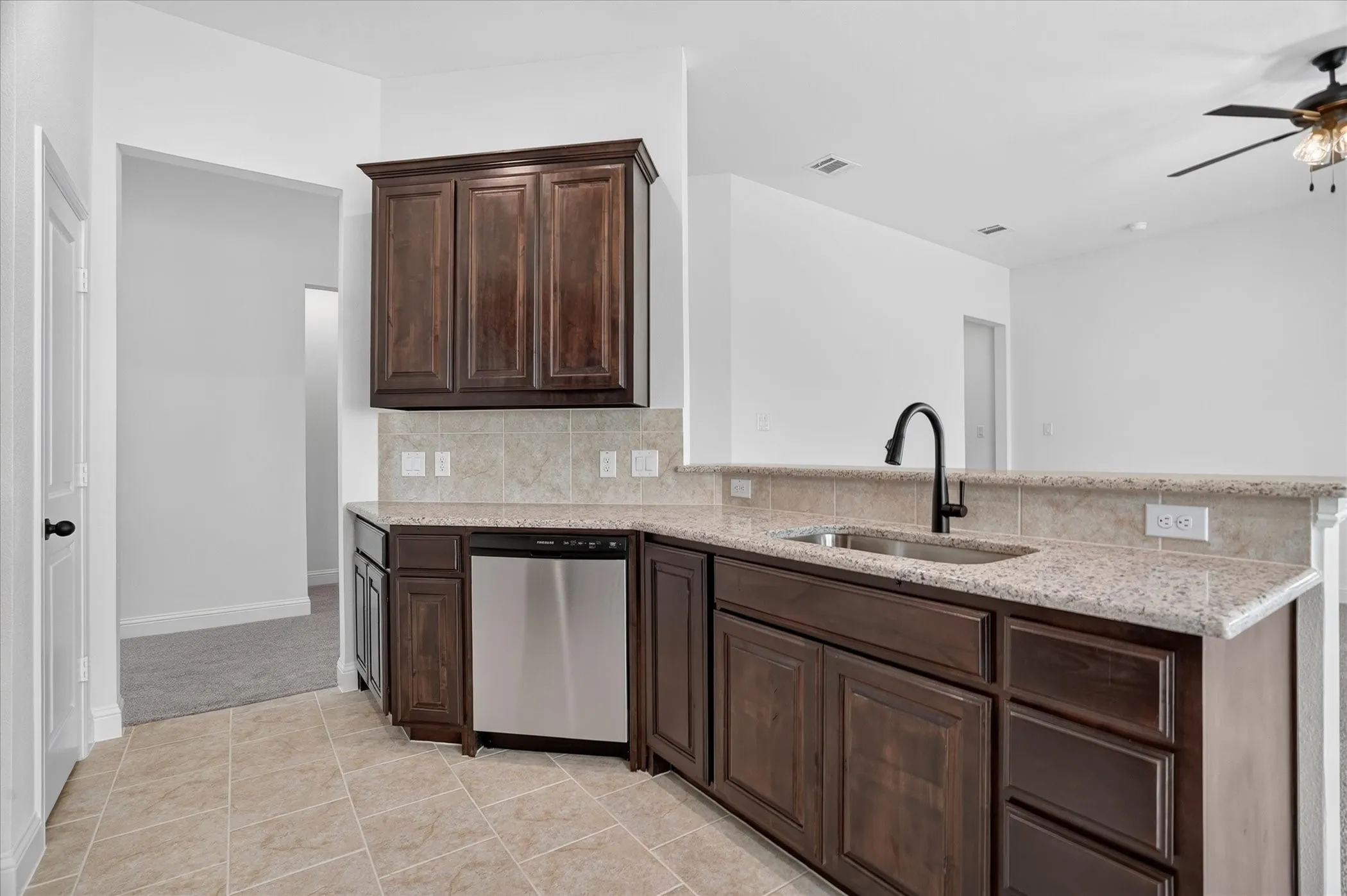 U-shaped kitchen island featuring dark wood cabinetry, light granite countertops, a stainless steel sink with a matte black faucet, a beige tile backsplash, and tile flooring