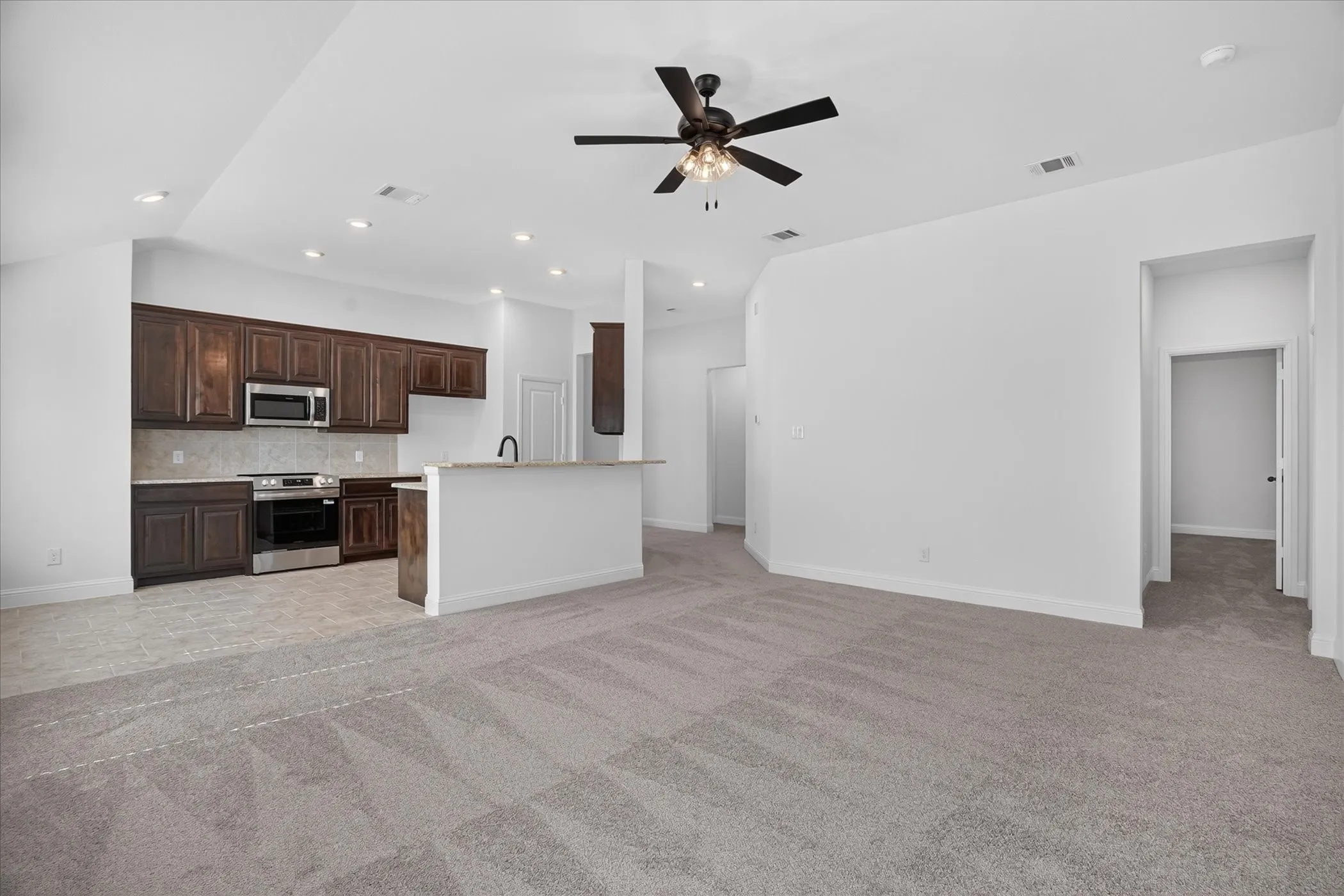Integrated kitchen and living area featuring dark wood-finish cabinetry, stainless steel appliances, and a central island