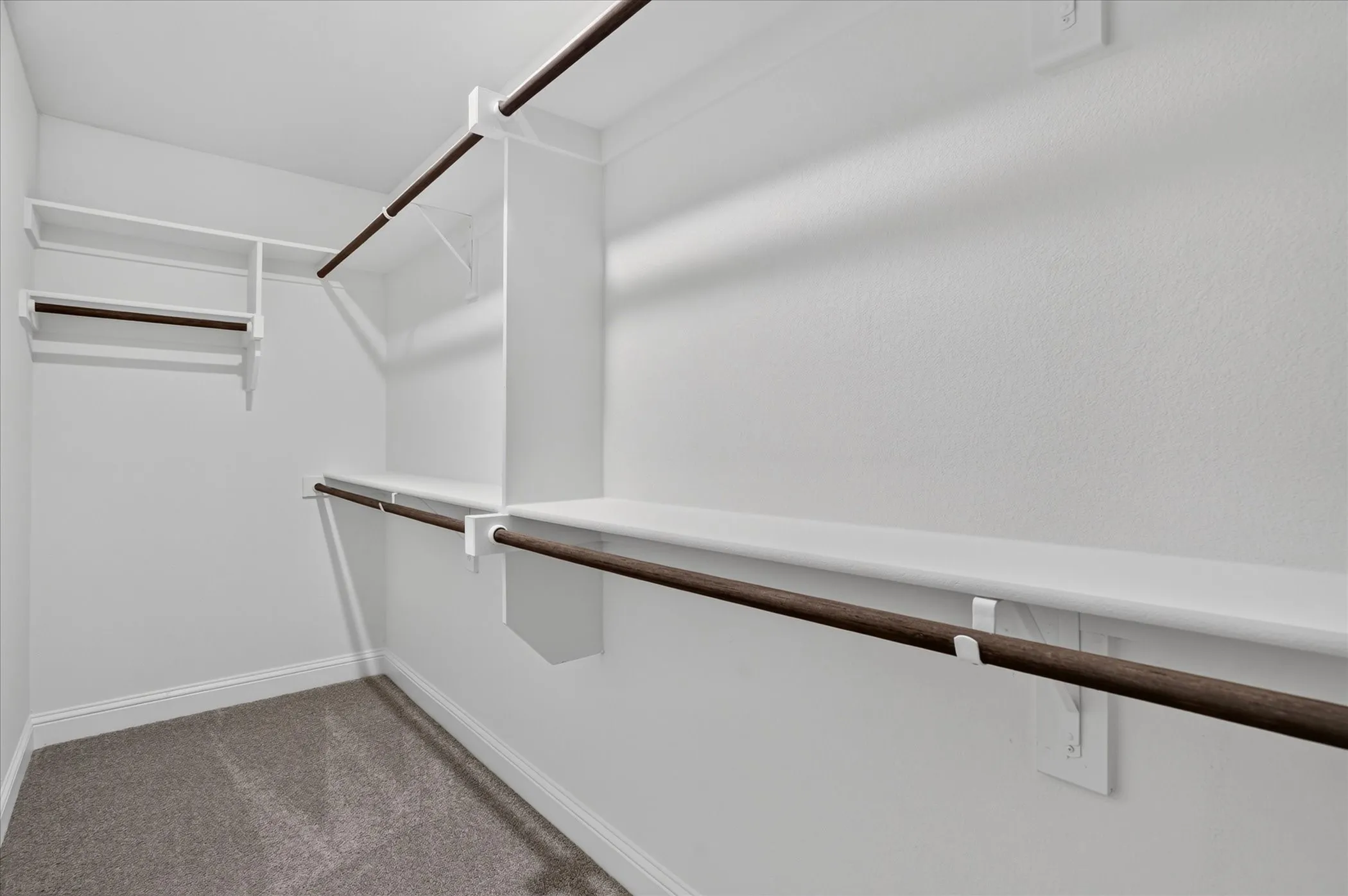 Wall-to-wall carpeting and white walls with multiple built-in shelving units and hanging rods