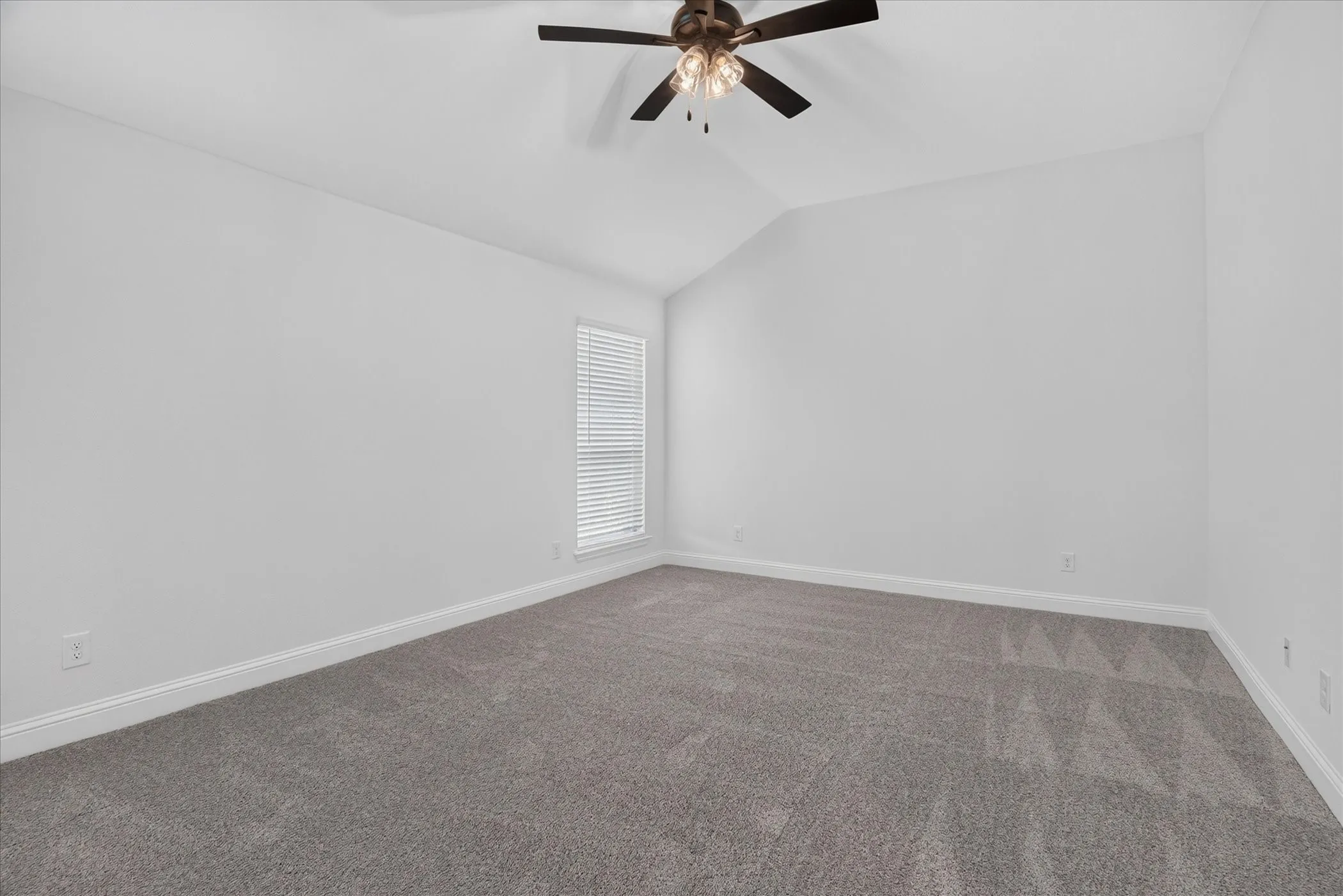 Vaulted ceiling with an integrated ceiling fan, carpeted flooring, and a window featuring horizontal blinds