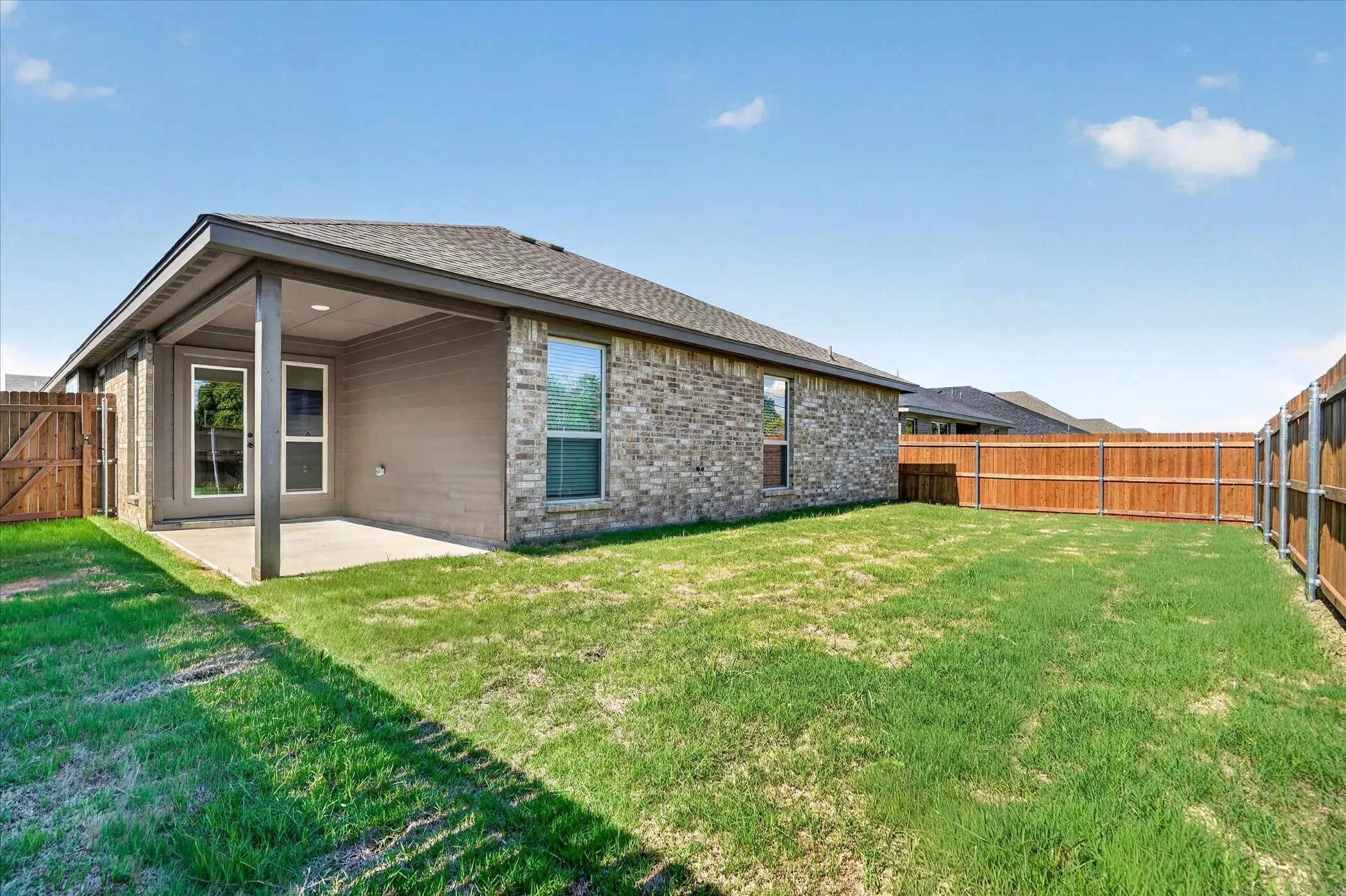 Expansive backyard featuring a covered patio with concrete flooring, full privacy fencing, and a brick exterior