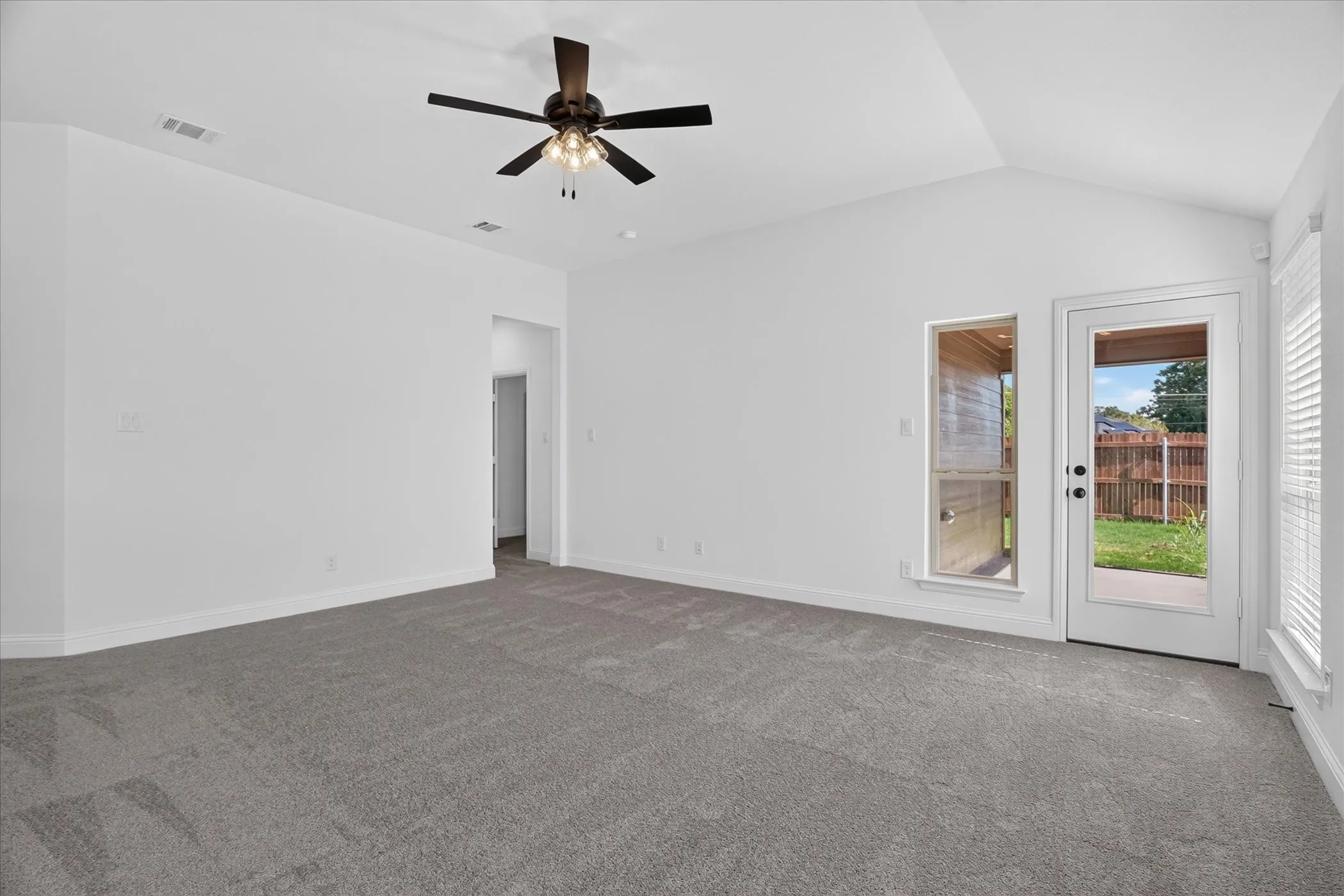 Vaulted ceiling, gray carpeting, ceiling fan with lighting, glass-paneled exterior door, and an exterior window