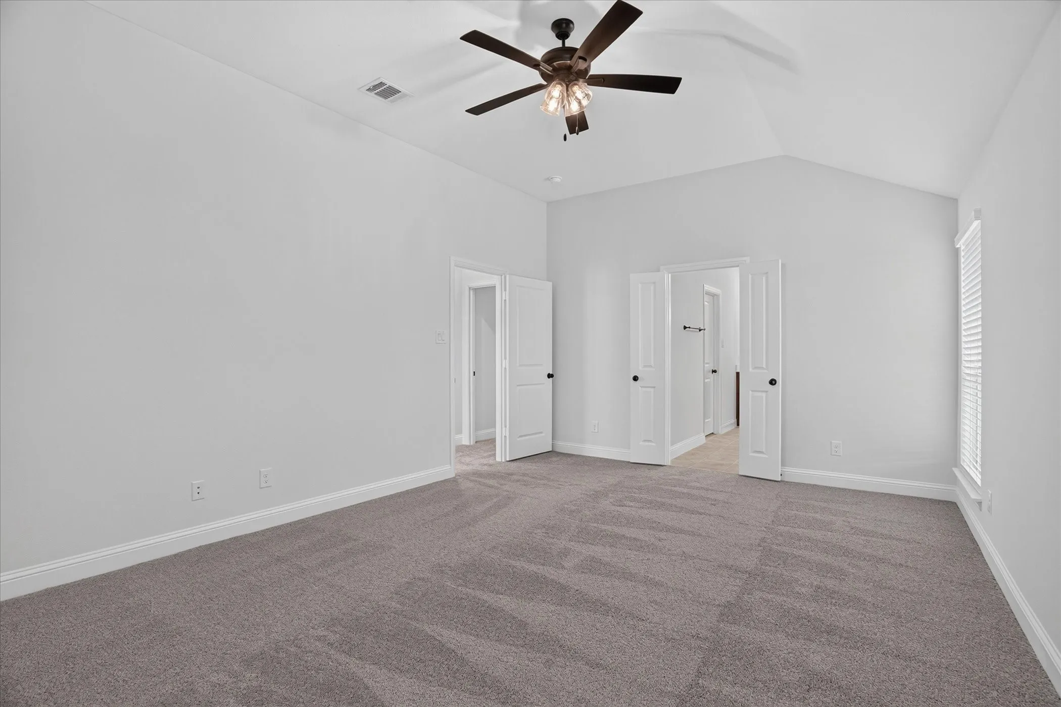 Vaulted ceiling, ceiling fan with integrated lighting, window with blinds, light gray wall paint, and gray carpeting