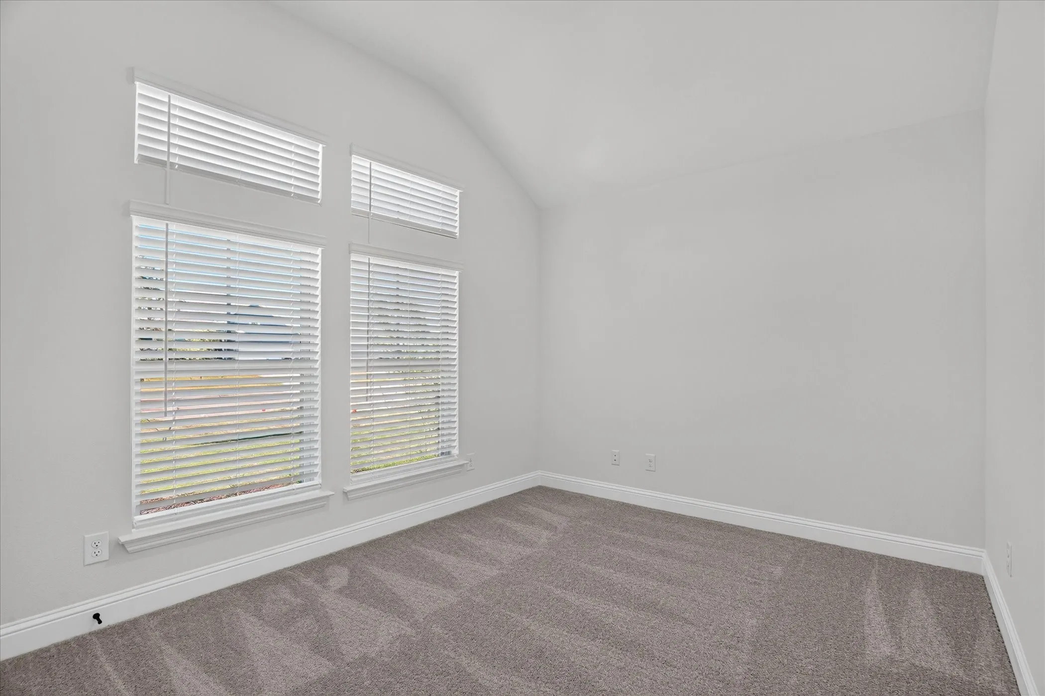 Vaulted ceiling featuring multiple windows with blinds and gray carpeting