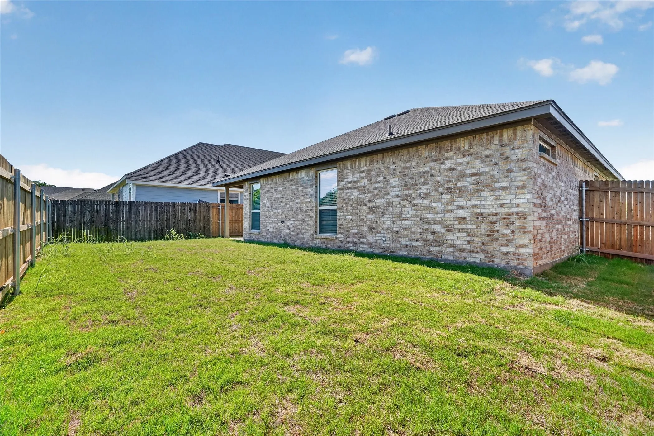 Expansive backyard with a manicured lawn, brick exterior, and a privacy fence