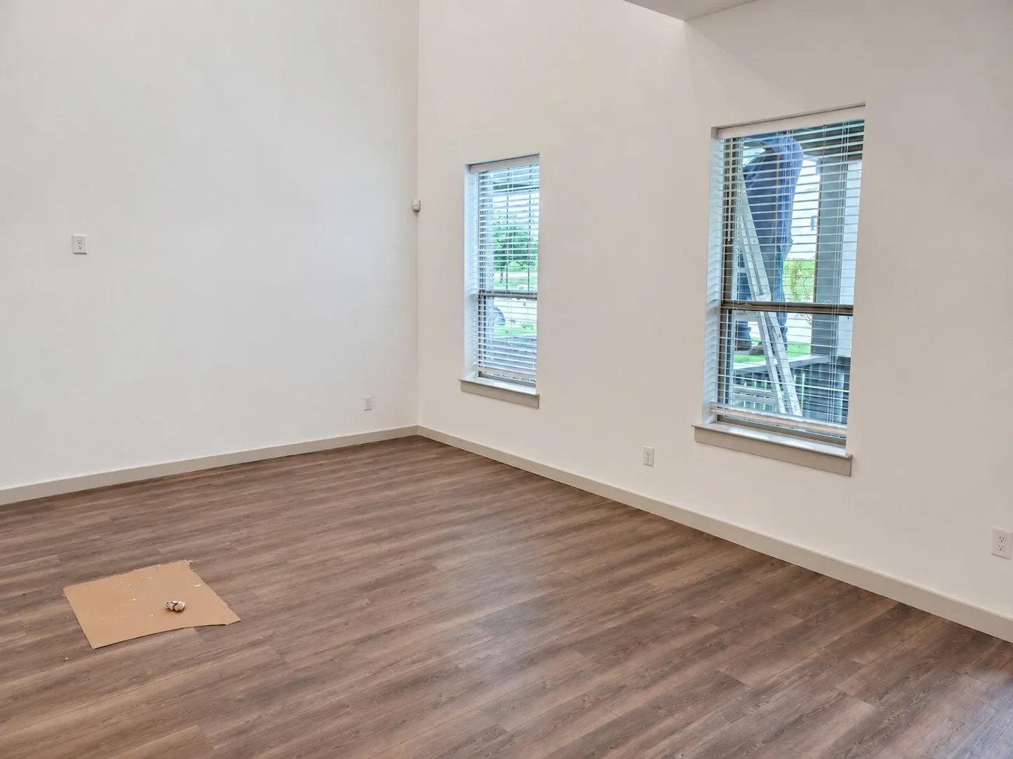 Vaulted ceilings, wood-finish flooring, white painted walls, and two windows with blinds