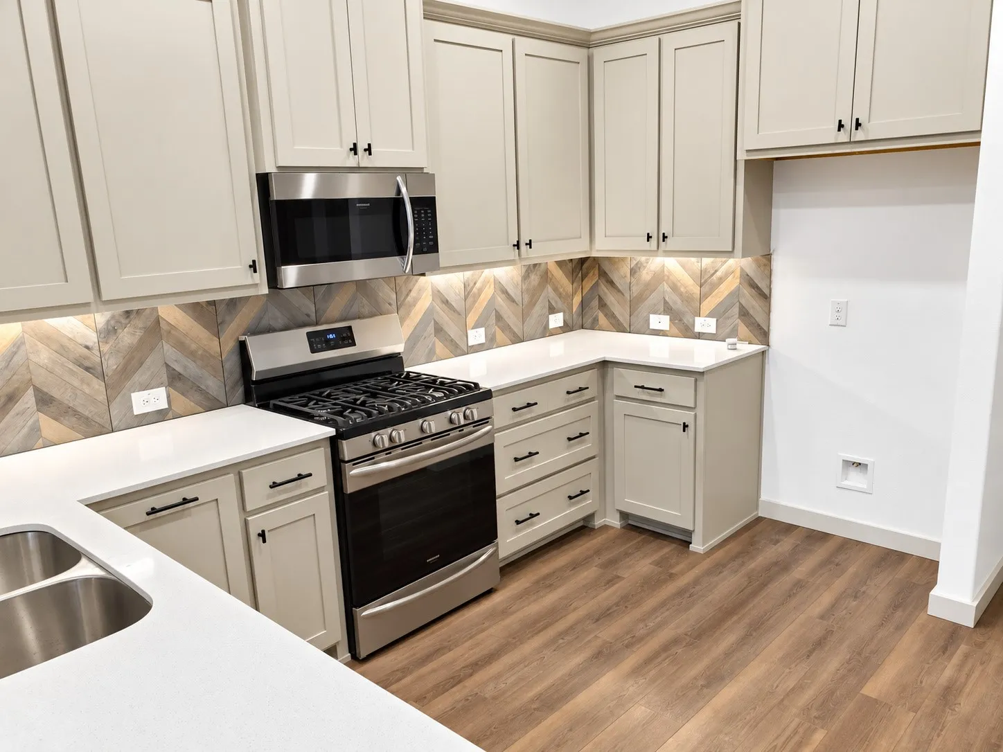 U-shaped kitchen with light-toned cabinetry, white countertops, stainless steel appliances, and wood-finish flooring