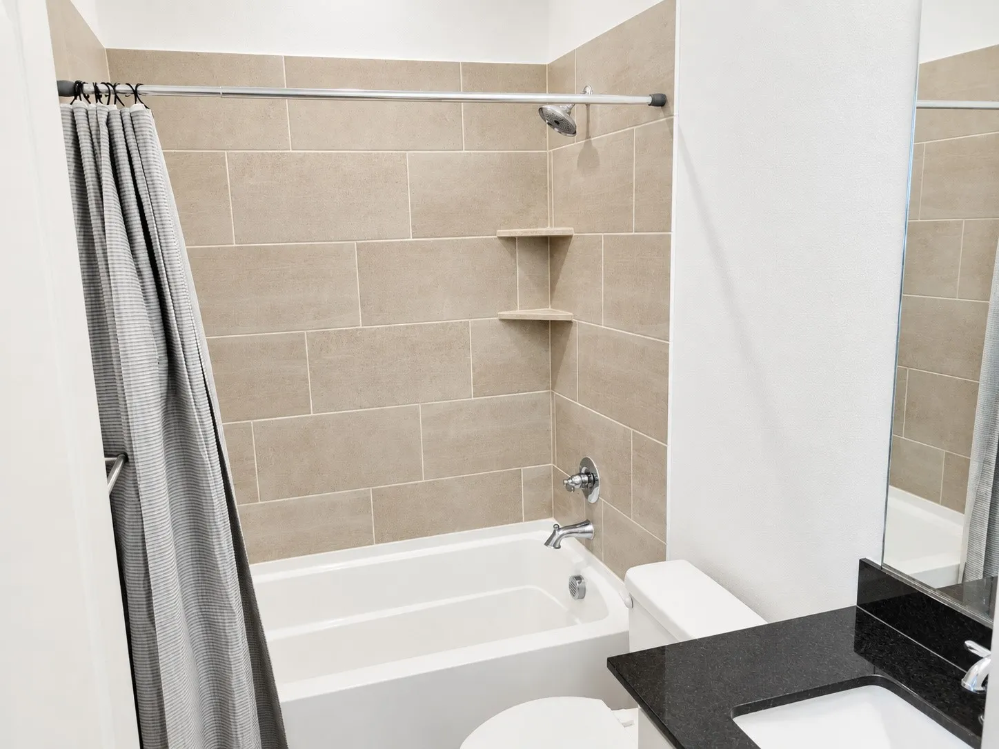 Shower-over-tub combination with ceramic tile surround, built-in corner shelving, and polished chrome fixtures
